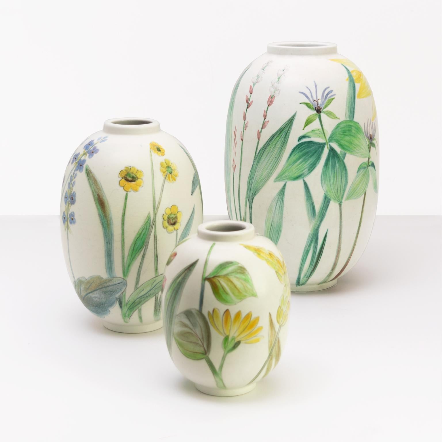 A group of 3 hand painted ceramic vases by Carl-Harry Stålhane decorated with flowers on a creamy white ground. Made at Rorstrand, Sweden, circa 1950. 

Measures: Heights: 11.5”, 8”, 6”, diameters: 7”, 6”, 4”.