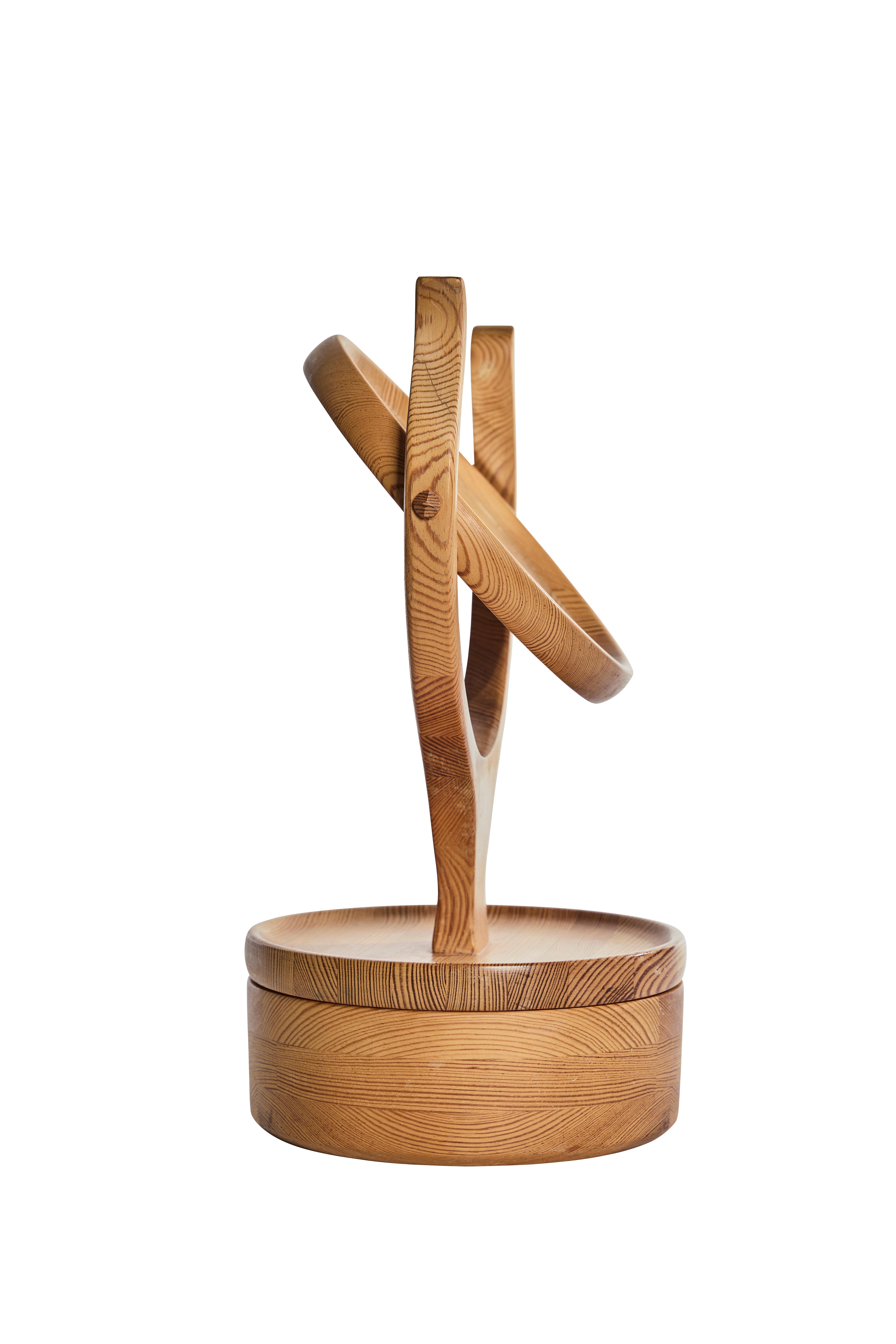 This sculptural Scandinavian Modern vanity mirror from the 1970s is a striking example of functional design and organic craftsmanship. Handcrafted in solid pine, the mirror features elegant curved arms supporting a circular pivoting mirror above a