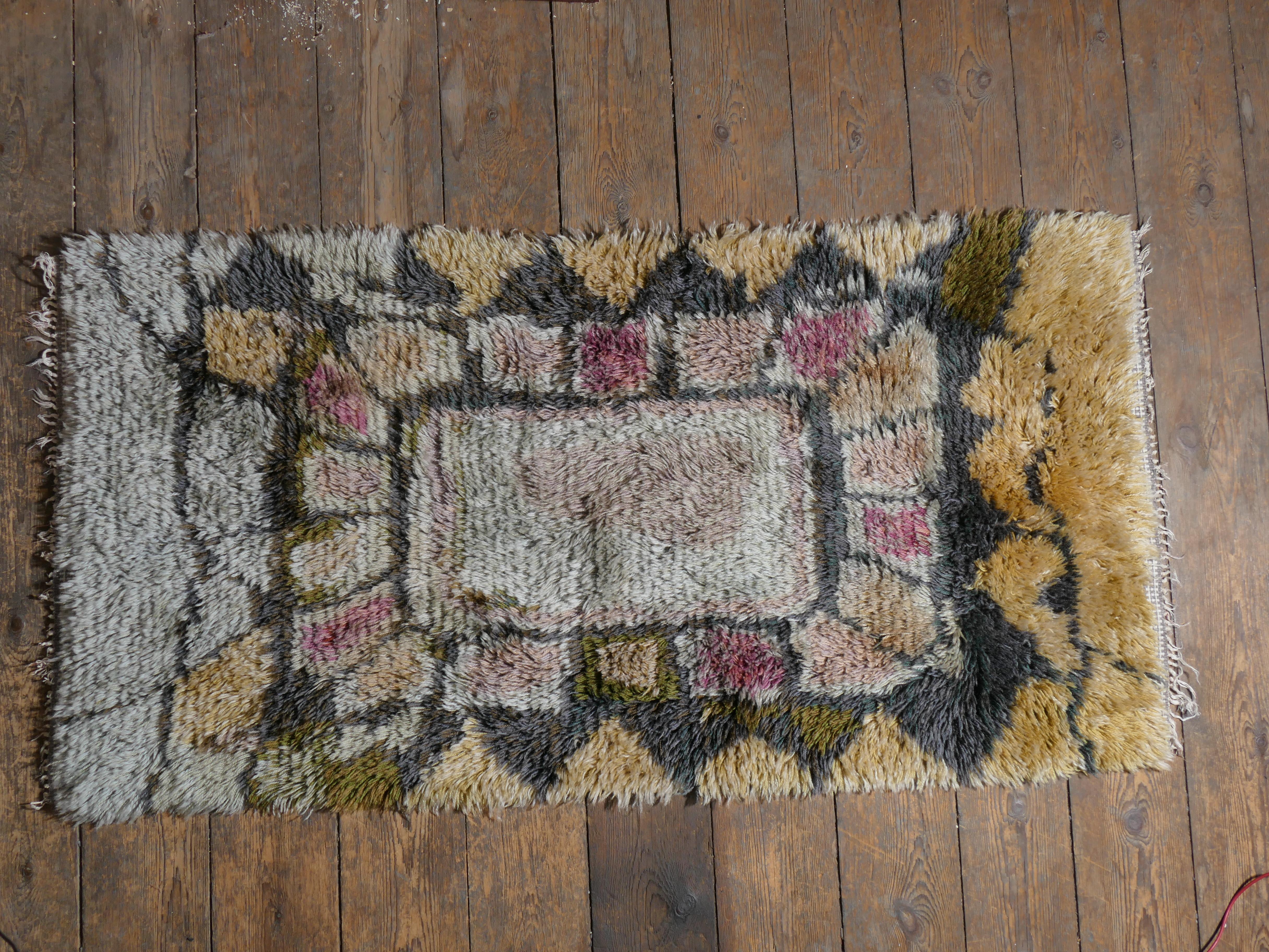 This is a very rare Scandinavian Modern high-pile wool rya rug has soft, muted natural tones of rose pink, wheat yellow, light and graphite grey, and moss green which brings a calm elegance to this versatile piece. The high pile creates a dynamic