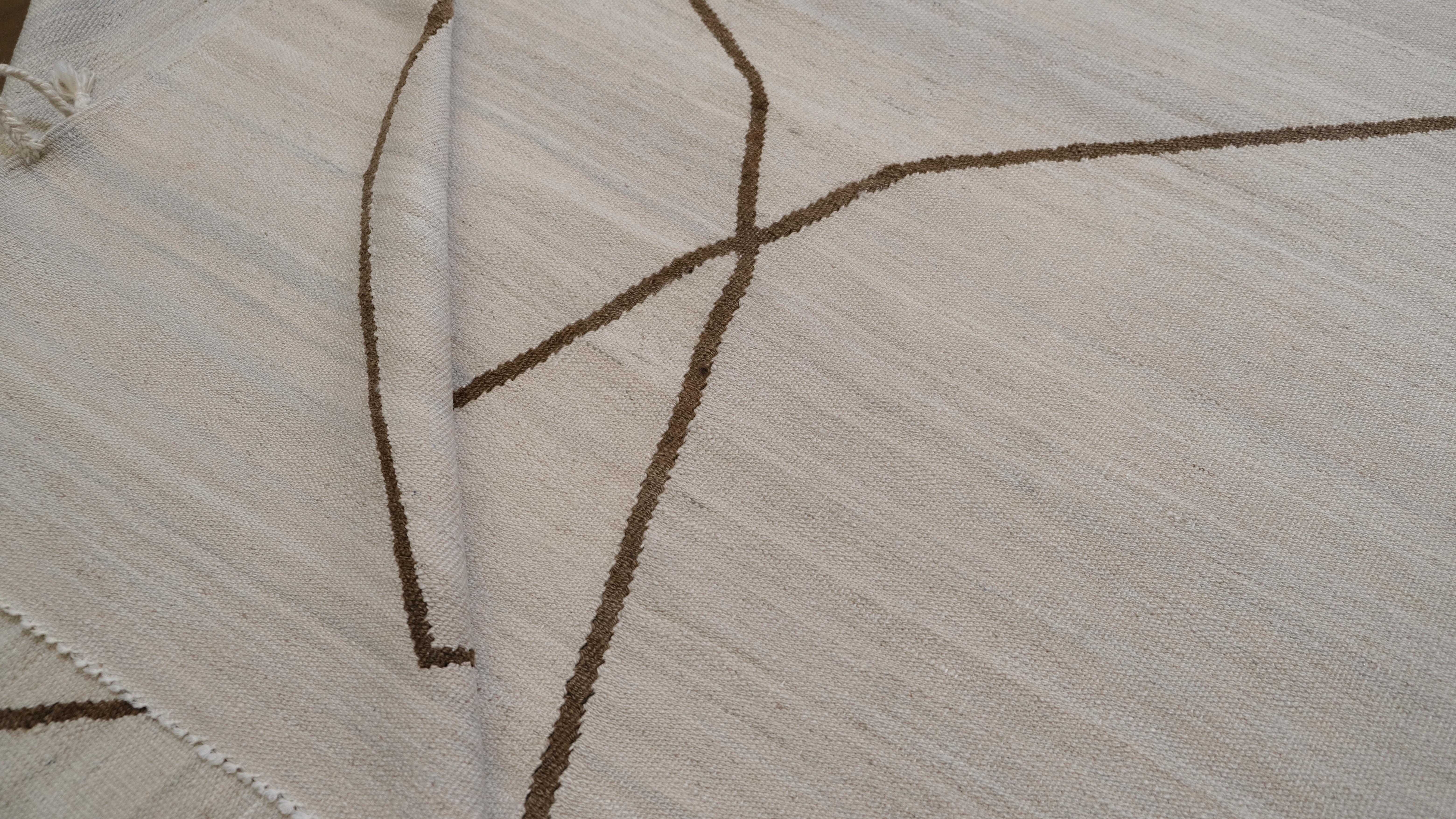 Eleganza sobria con questo tappeto in lana intrecciata a mano. Con un morbido sfondo beige ornato da delicati motivi lineari marroni, questo tappeto incarna il minimalismo e la raffinatezza. Le linee astratte che si intersecano creano un fascino