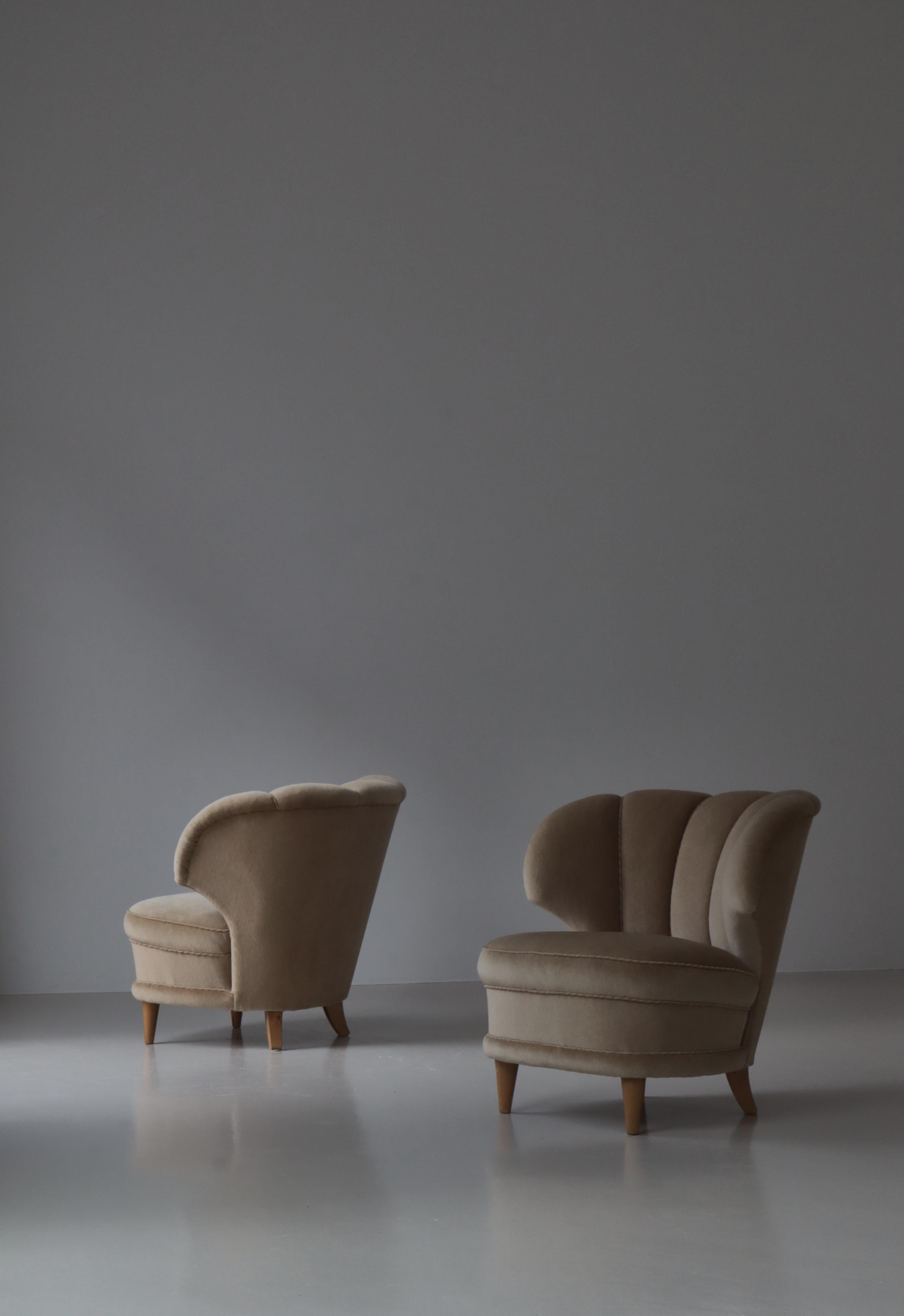 A pair of lounge chairs designed by Carl-Johan Bowman in Finland in the 1940s. The chairs are upholstered in beige suede. Legs of solid birchwood. 
Carl-Johan Boman (1883 - 1969) was a Finnish designer. He designed furniture for his company Oy Boman