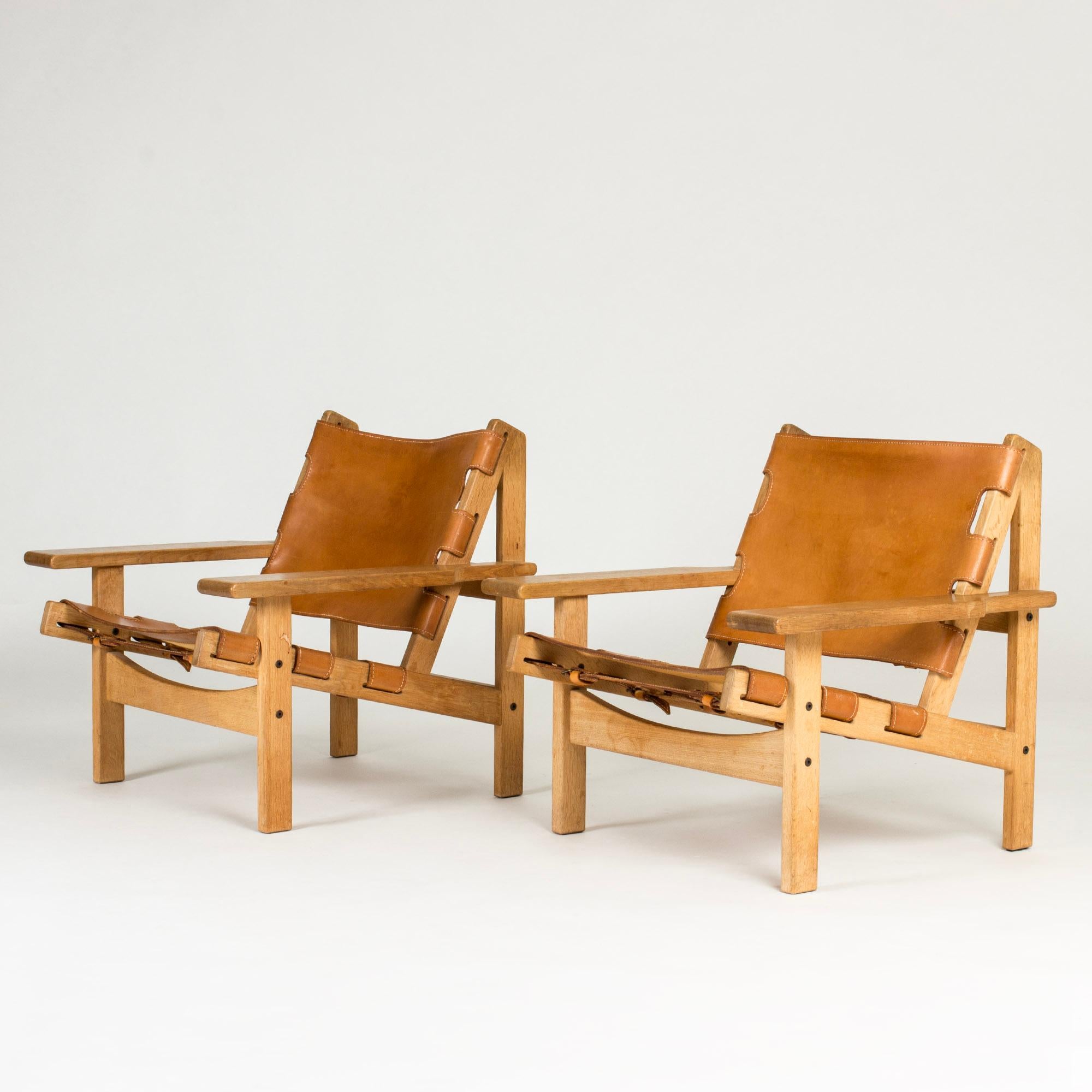 Pair of cool hunting chairs by Kurt Østervig, model 168. Made from oak with distinct lines, cognac colored leather with decorative straps in the back.