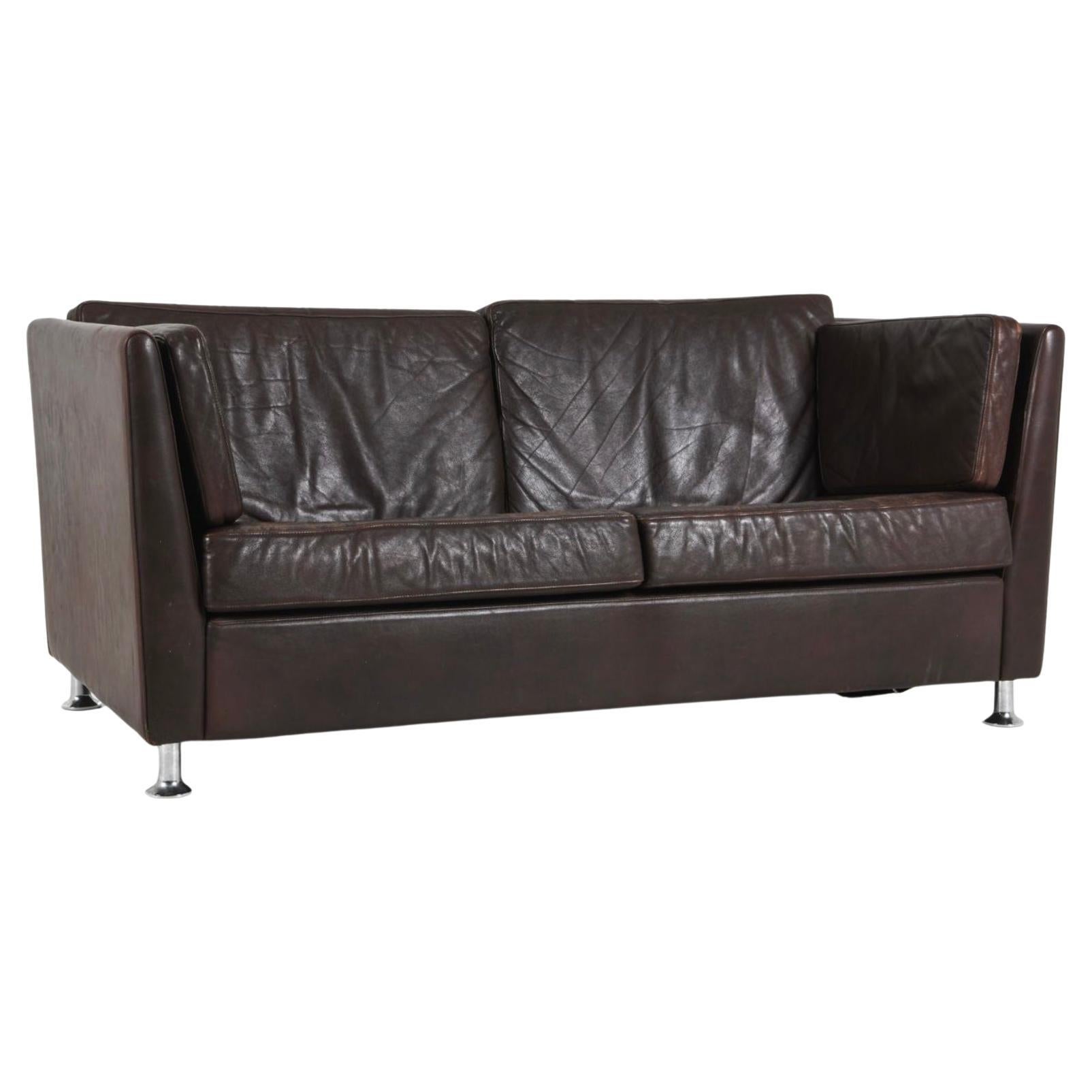 Sofá Loveseat escandinavo moderno bajo de cuero marrón con patas cromadas. La tapicería de cuero marrón, con una hermosa pátina, muestra el desgaste normal y el paso del tiempo. Pies metálicos en acabado cromado. Fabricado en Dinamarca, hacia