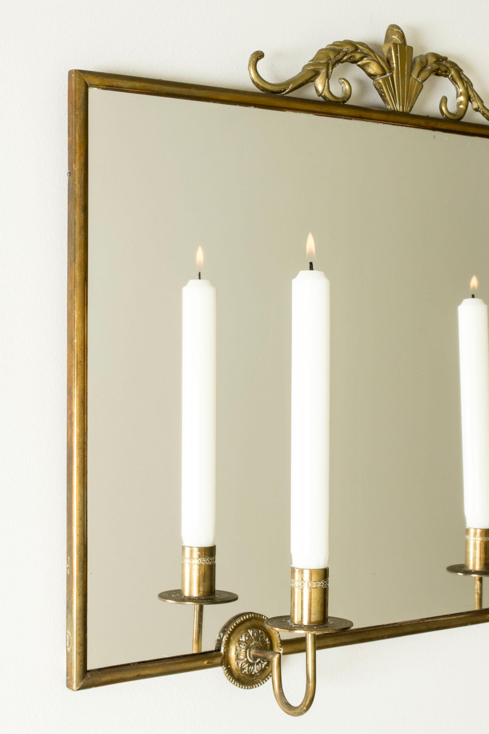 Precioso espejo de Lars Holmström, de forma limpia, con dos candelabros de latón. Adornado con un bonito lazo en la parte superior.