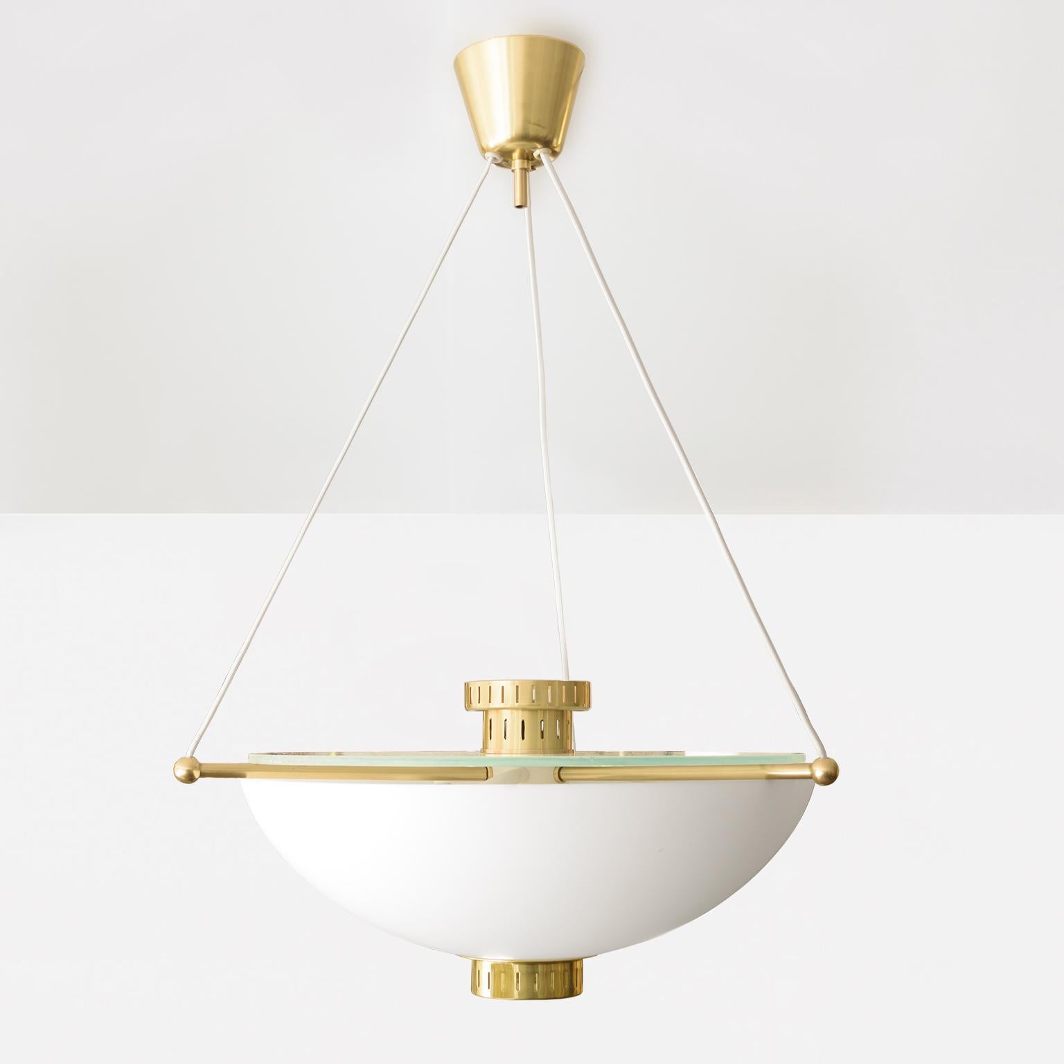 Un elegante apparecchio a sospensione di stile moderno scandinavo con un paralume in vetro opalino a mezza sfera. L'apparecchio è sospeso con cavi elettrici in seta che si estendono da tre bracci in ottone e si incontrano in un baldacchino in ottone