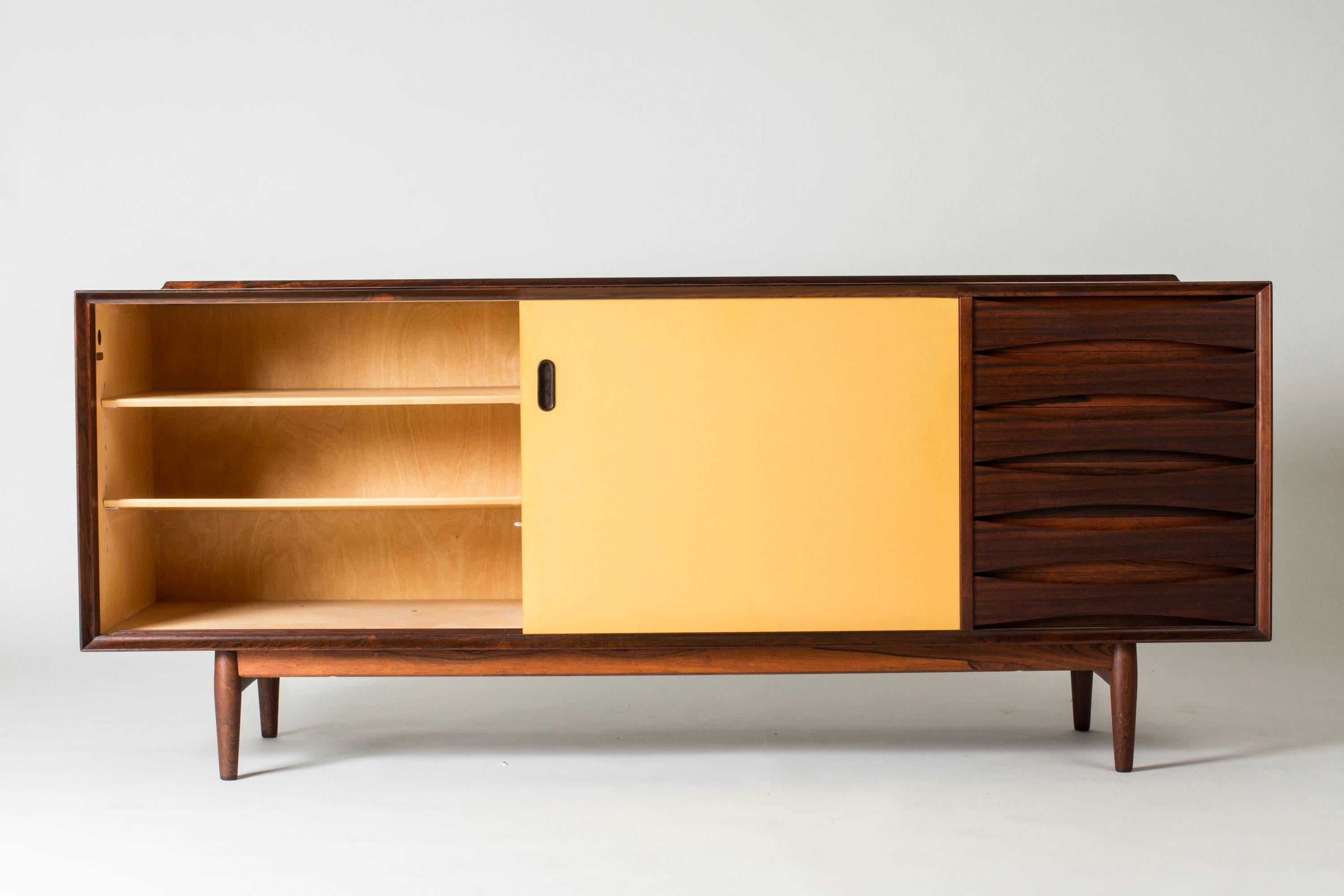 Beautiful “OS29” rosewood sideboard by Arne Vodder, where yellow and white panel doors contrast with the cleanly sculpted drawers to the right. A rim runs along the back of the table top.