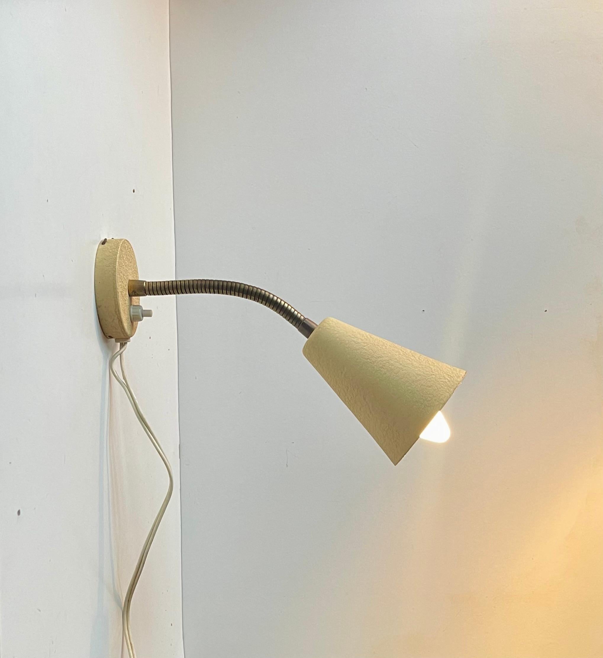 Fully adjustable wall lamp made from Aluminium applied with a 1950s characteristic pastel yellow leather-like texture paint (all original). The flexible goose-neck is made from brass. Very clean almost NOS condition and very rare to find a 1950s