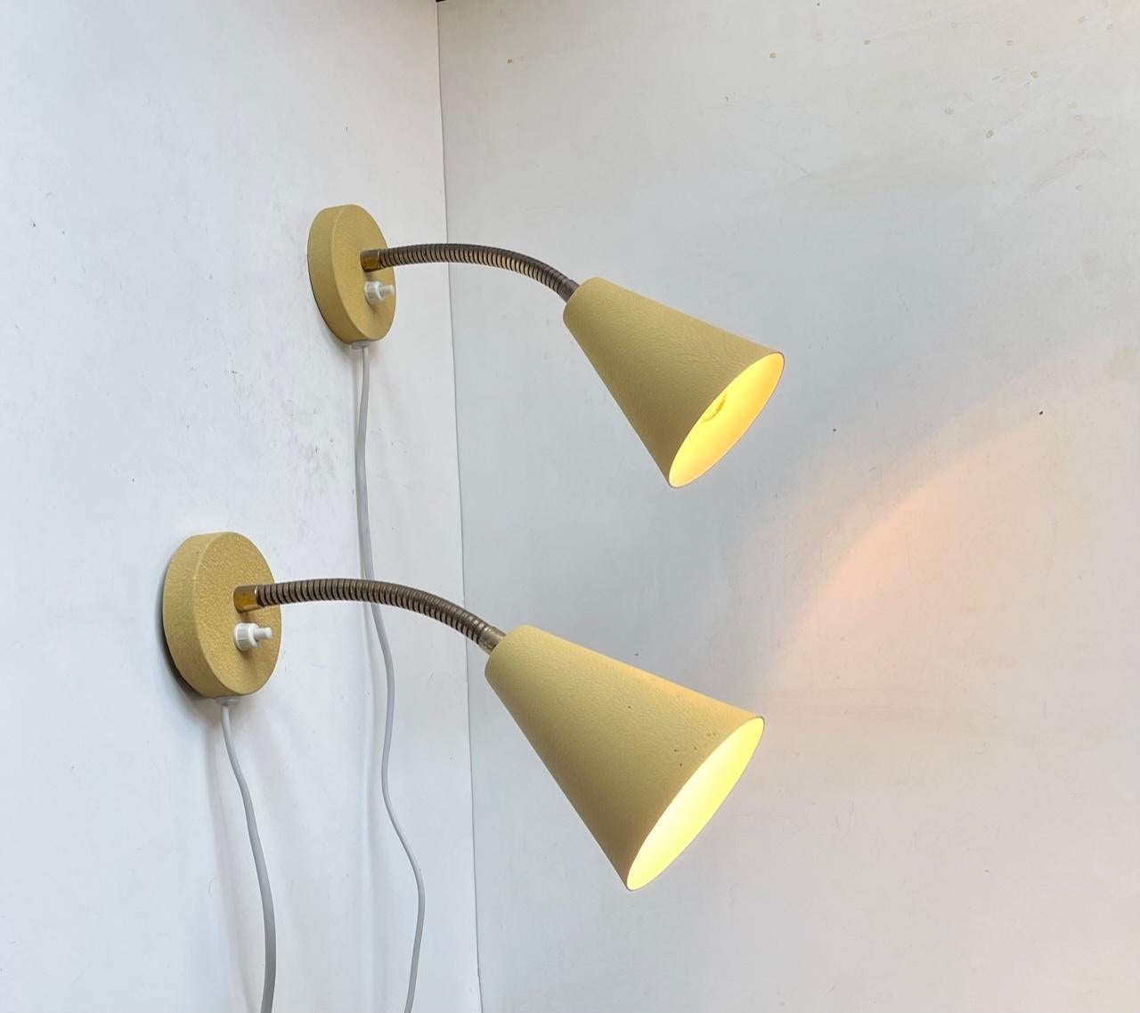 Fully adjustable wall lamps made from Aluminium applied with a 1950s characteristic pastel yellow texture paint (all original). The flexible goose-necks are made from brass. Very clean almost NOS condition and very rare to find 1950s sconces this