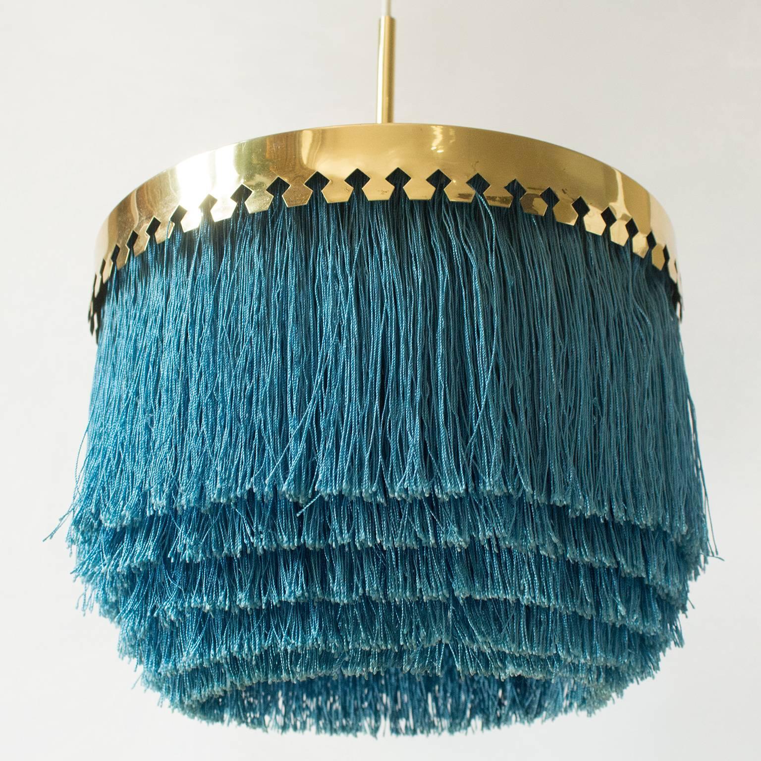 The one and only iconic pendant lamp with cut brass canopy with blue/green colored silk fringes. Wonderful condition and its original, still in line with age to both the brass and the silk. Created in 1960 by the acclaimed Swedish lighting genius,
