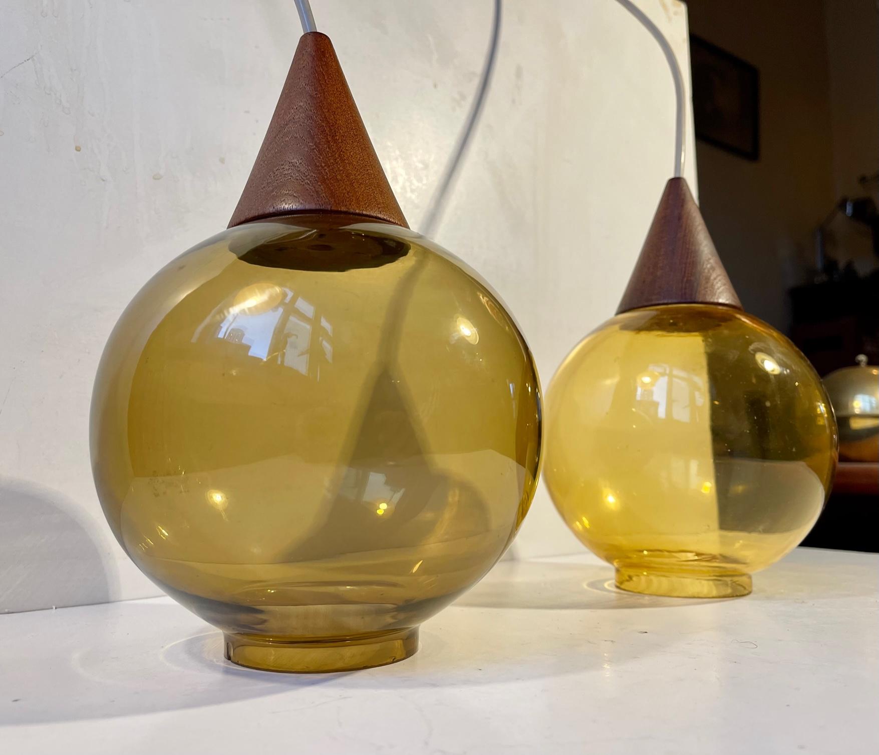 Unusual hanging pendant lights that resembles some of Hans Agne Jakobsson´s designs. Made from colored mouth-blown smoke glass and set in conical teak tops. The glass shades has diffrent color tones (one olive green and one amber yellow). Made by an