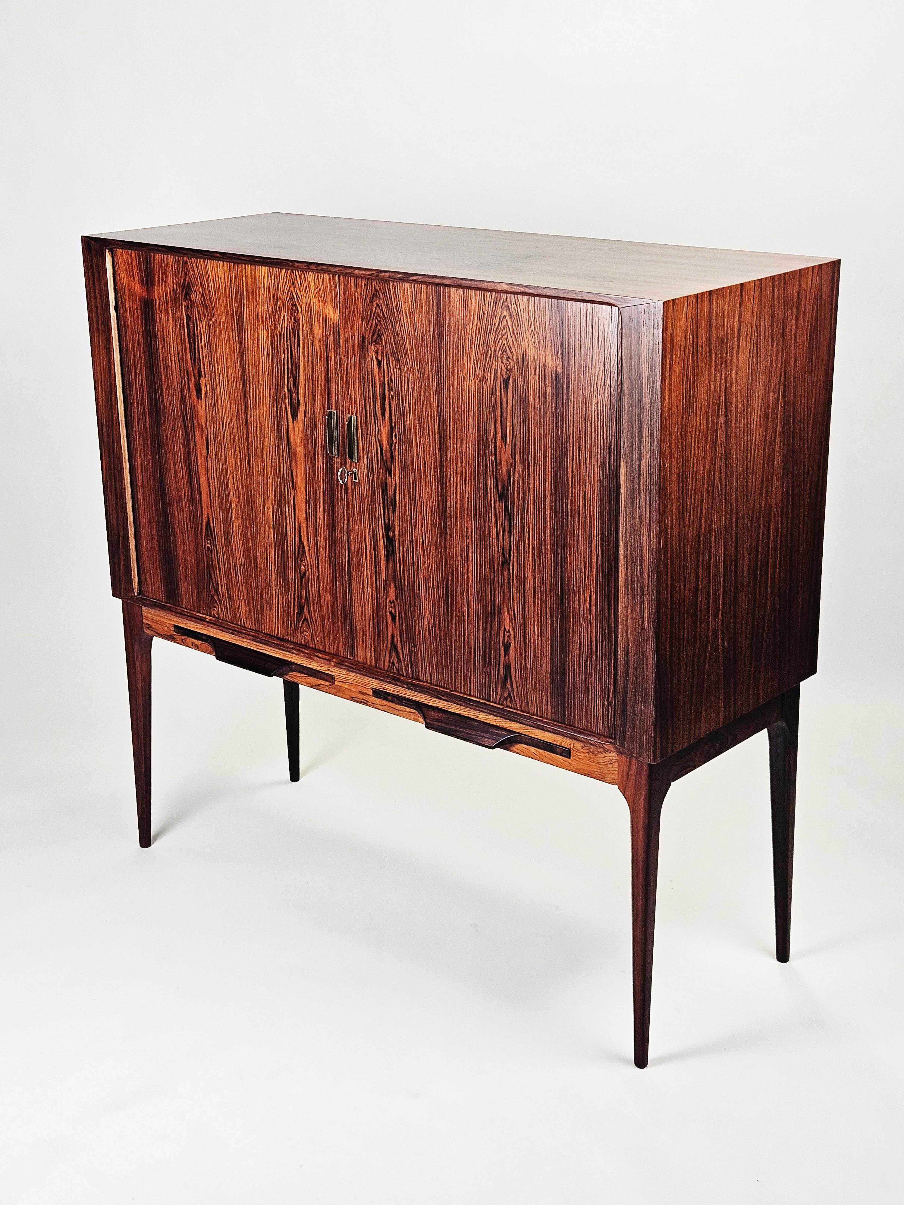 Magnifique meuble de bar conçu par Kurt Østervig au Danemark dans les années 1960. 

Fabriqué en bois de rose avec des portes à jalousie, des détails en laiton et des détails élégants en laiton. 