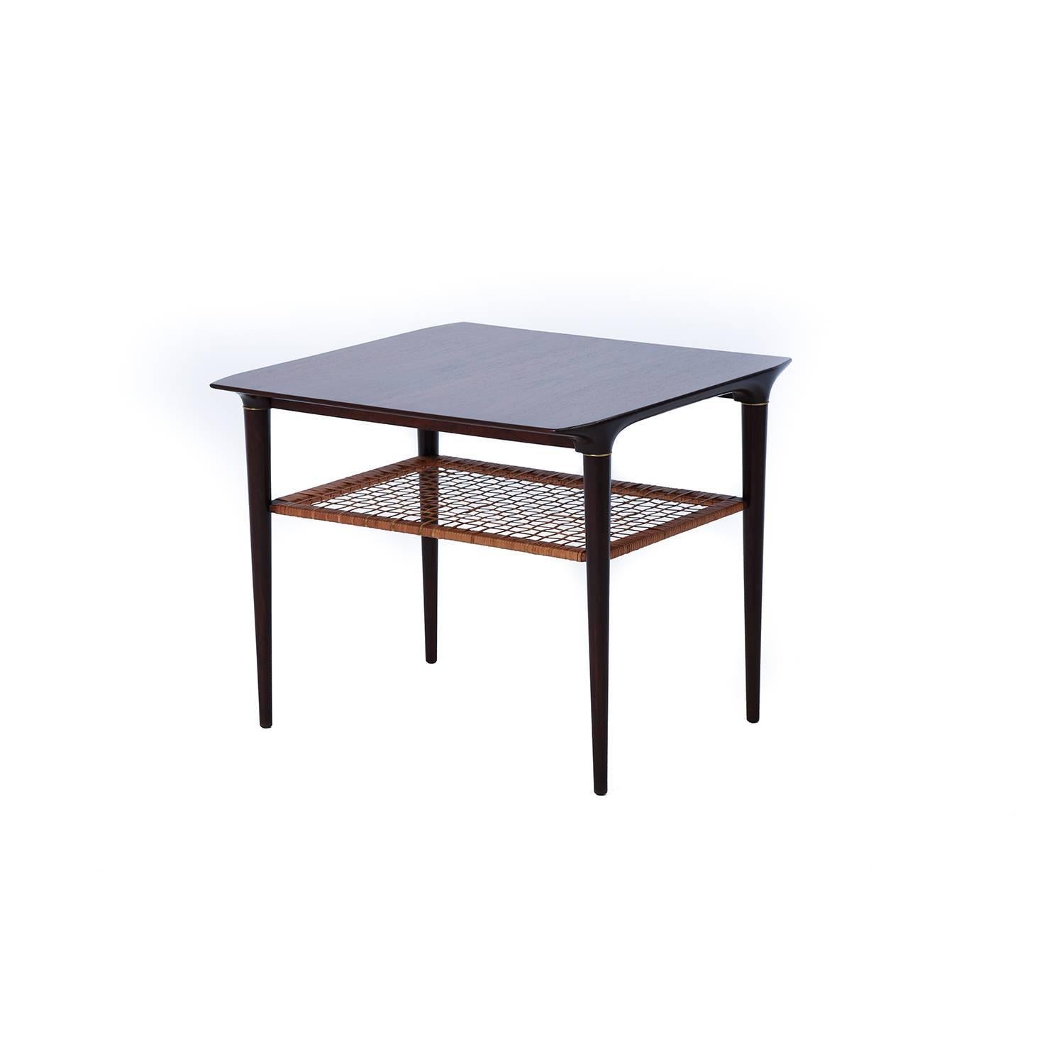 This elegant corner table is a Classical example of Danish modern rosewood, with a deeply figured grain pattern on the surface. Cane shelf and brass ring details. Lacquer finished.