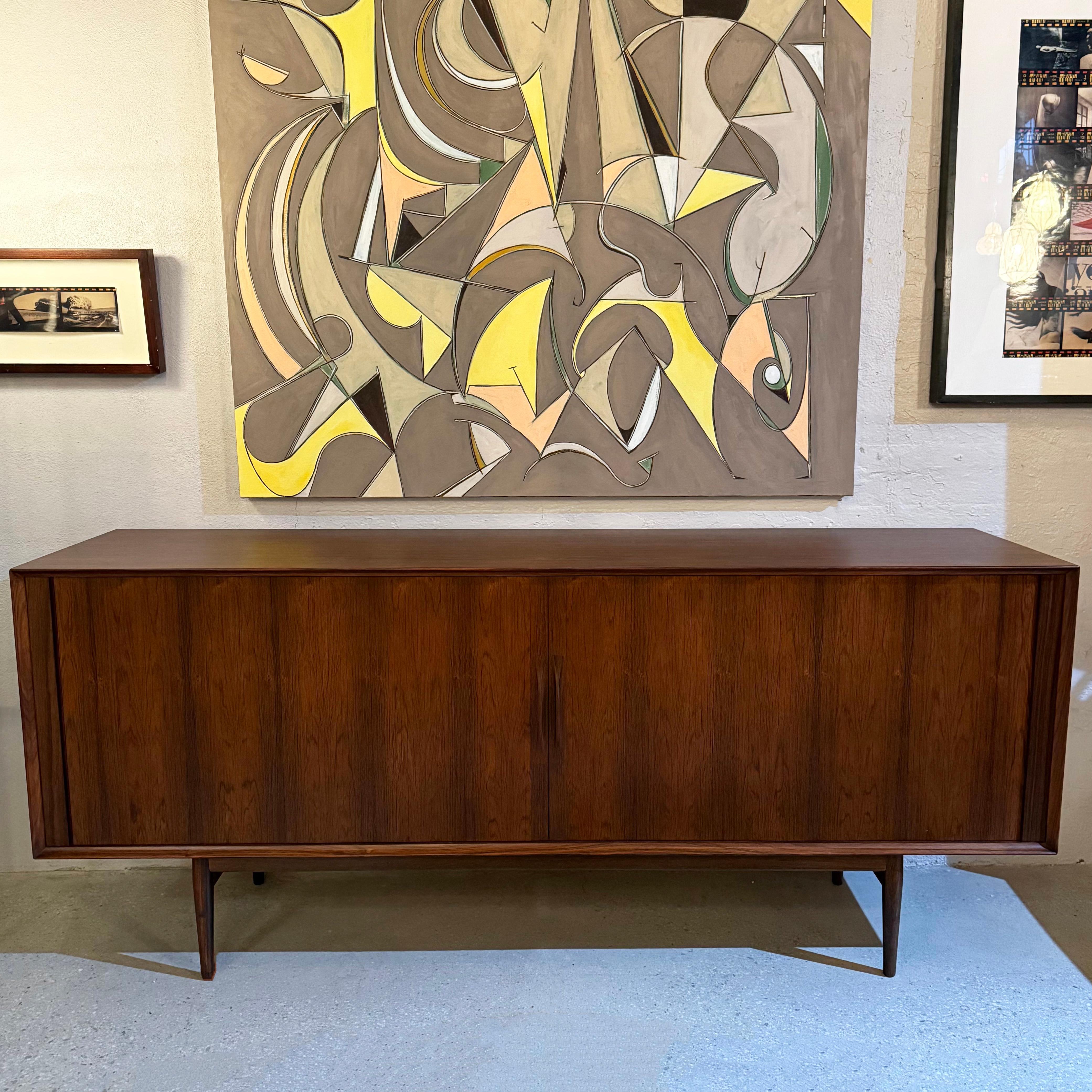 This streamlined Scandinavian Modern rosewood credenza / sideboard is by Danish designer Arne Vodder for Sibast. It features a stunning rosewood grain throughout with sleek tambour doors and sculpted handles that open to reveal adjustable interior