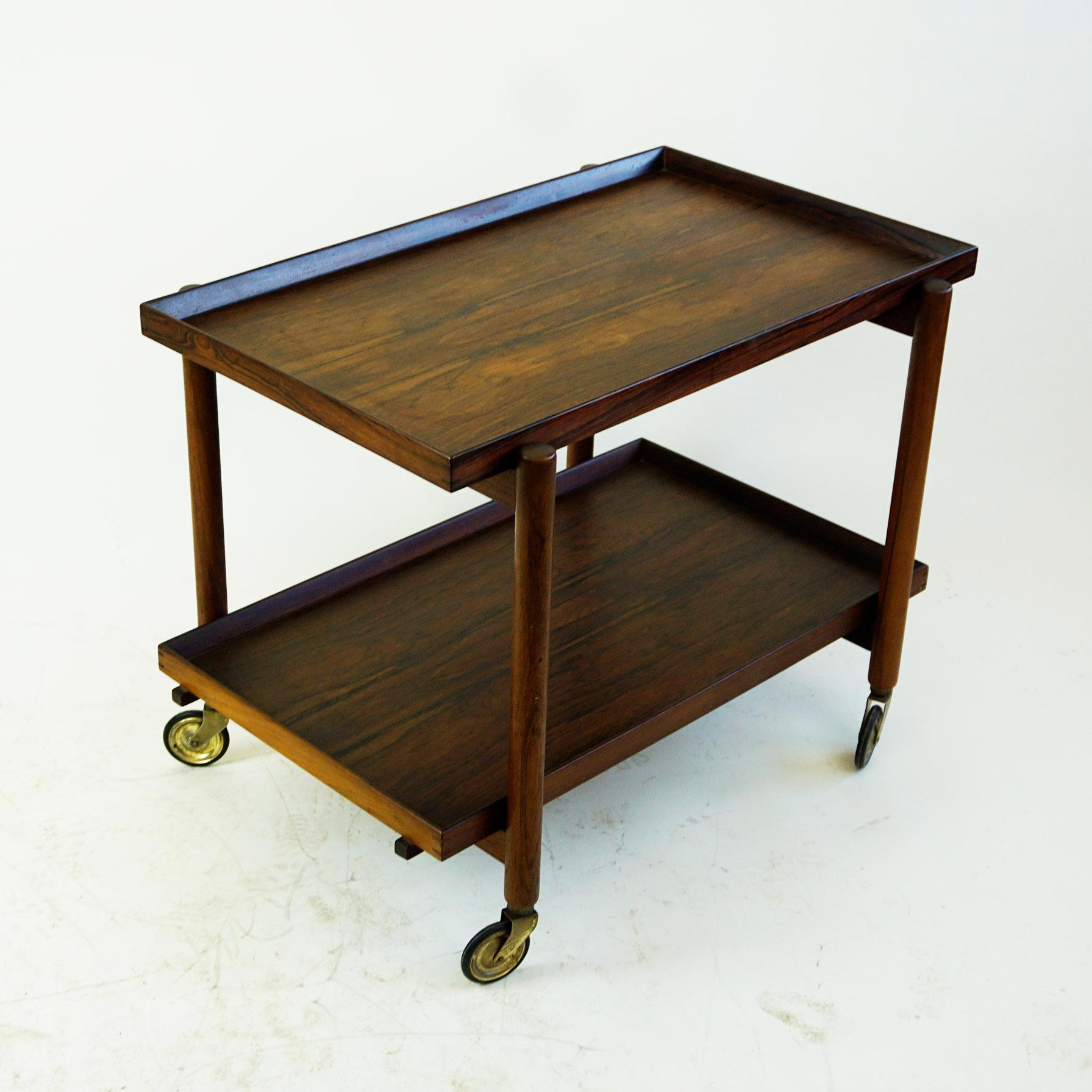 Vintage Scandinavian Modern Poul Hundevad rosewood bar cart from the 1960s. This unique design allows for the bottom tray to be removed and added to the top to expand the serving surface.
Brass and rubber casters. Expands to 60 inches when bottom