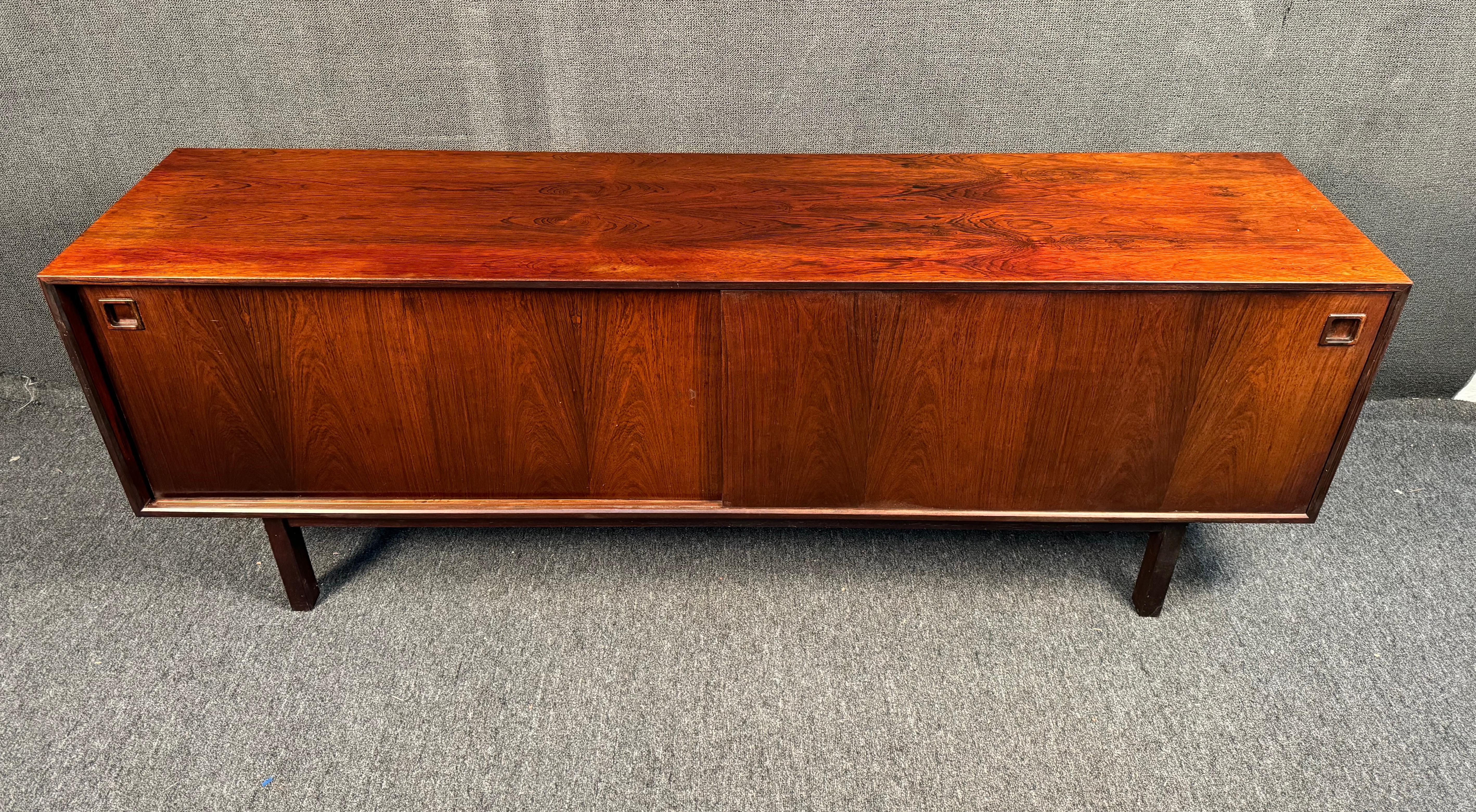 The elegant modern style of Scandinavian designer Gunni Oman sets this sliding door Rosewood sideboard apart from other Mid-Century servers. Featuring four felt lined drawers, spacious cabinet space, and rich vintage finish this unique piece for