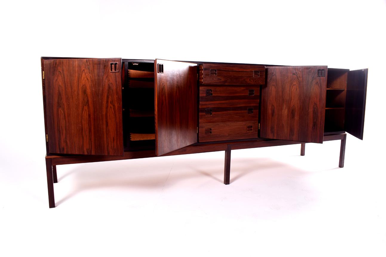 Midcentury rosewood sideboard designed by Johannes Andersen for Bernhard Pedersen & Son, Denmark. Model 160, features recessed square pulls. The cabinet has four drawers in center and doors on either side. Mahogany interior with adjustable shelves