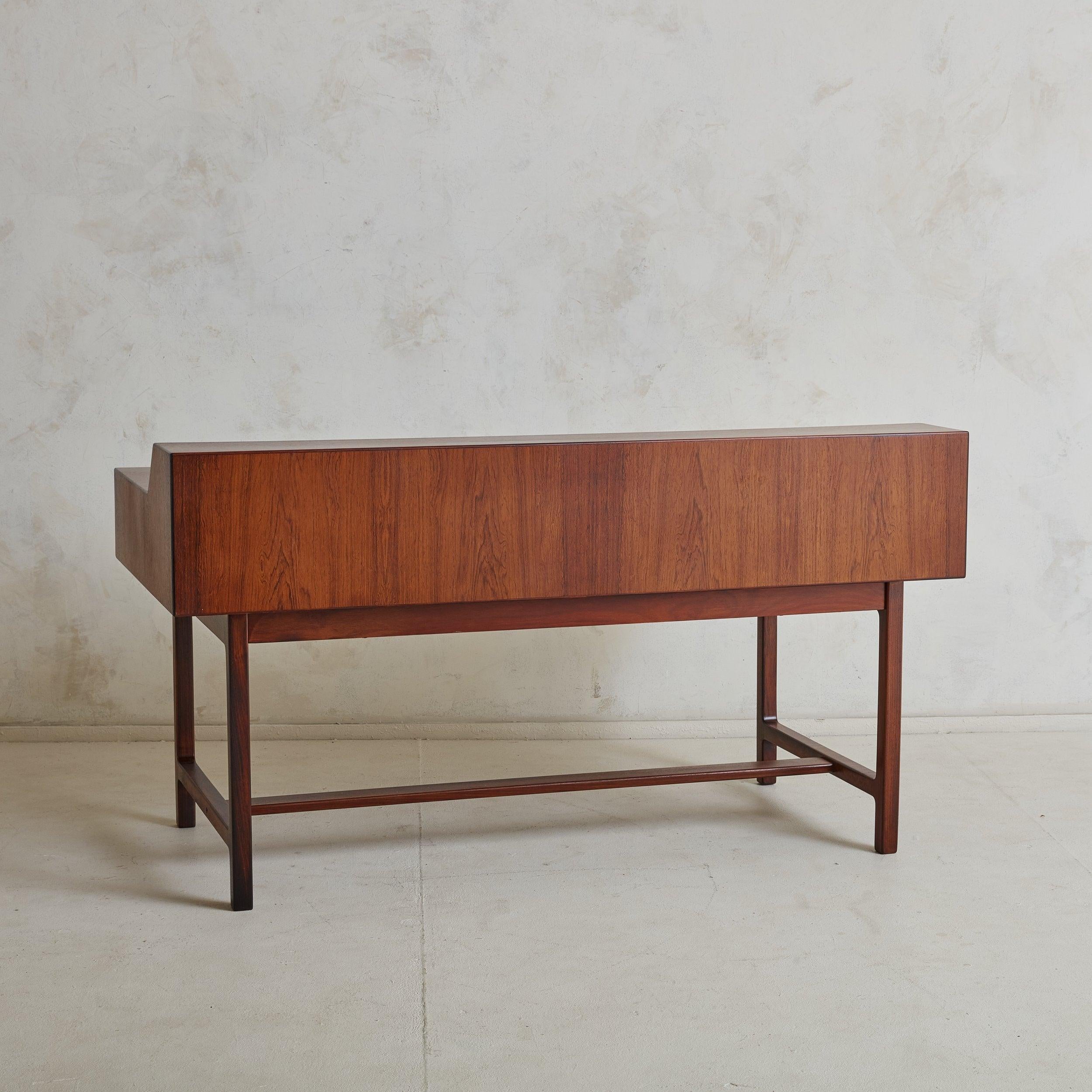 A rare Scandinavian Modern writing desk constructed of rich, solid rosewood with gorgeous graining. The striking, yet minimal design features a rectangular surface accented with an inset black leather writing pad and spacious raised shelf. This desk