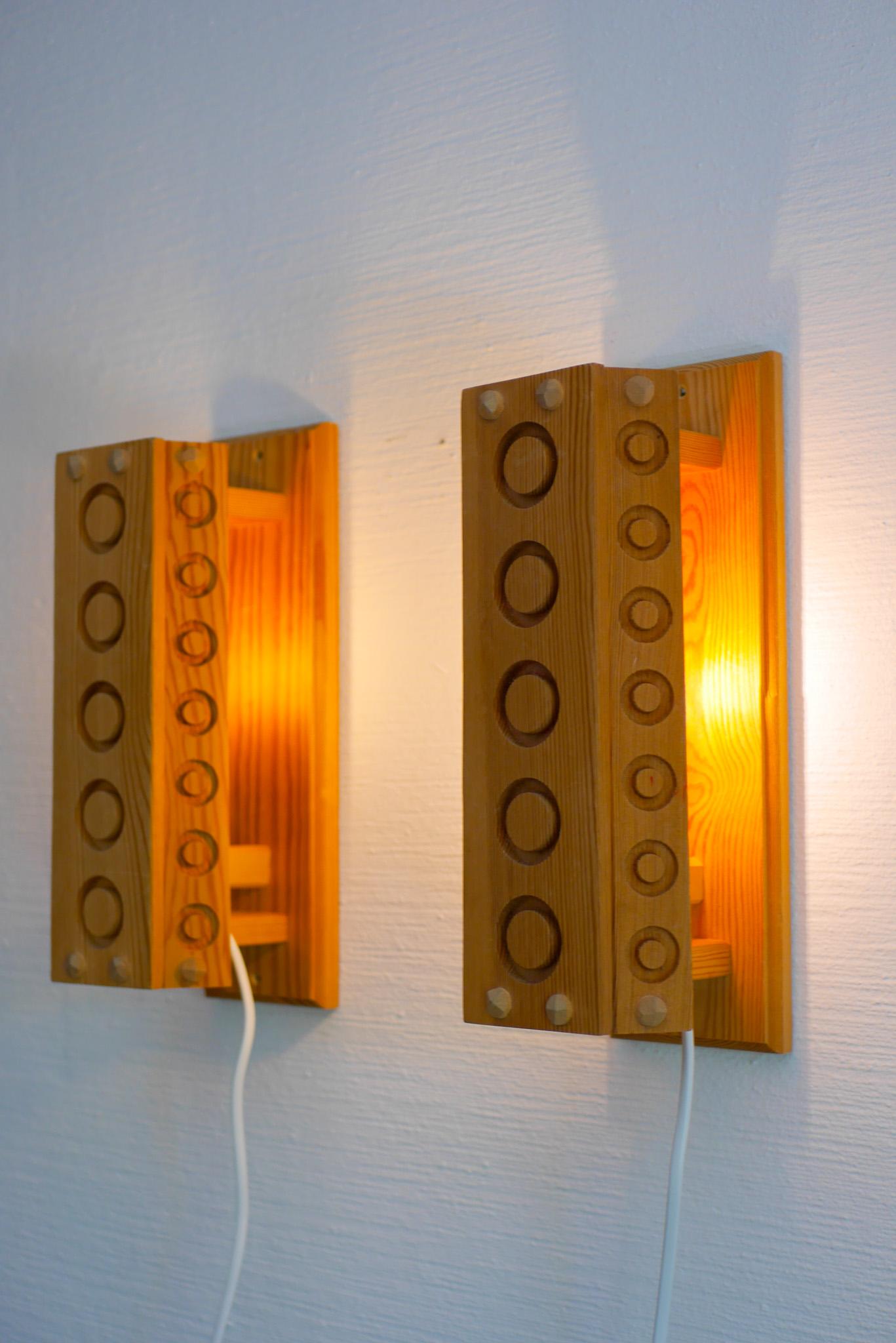 A oair of vintage mid-century modern Swedish wall lights or sconces made from Pine wood. Made by Stig Sandqvist in the 1970s with a very simple yet equally fantastic design. At the front and sides, the lamps have circles in the wood and on each