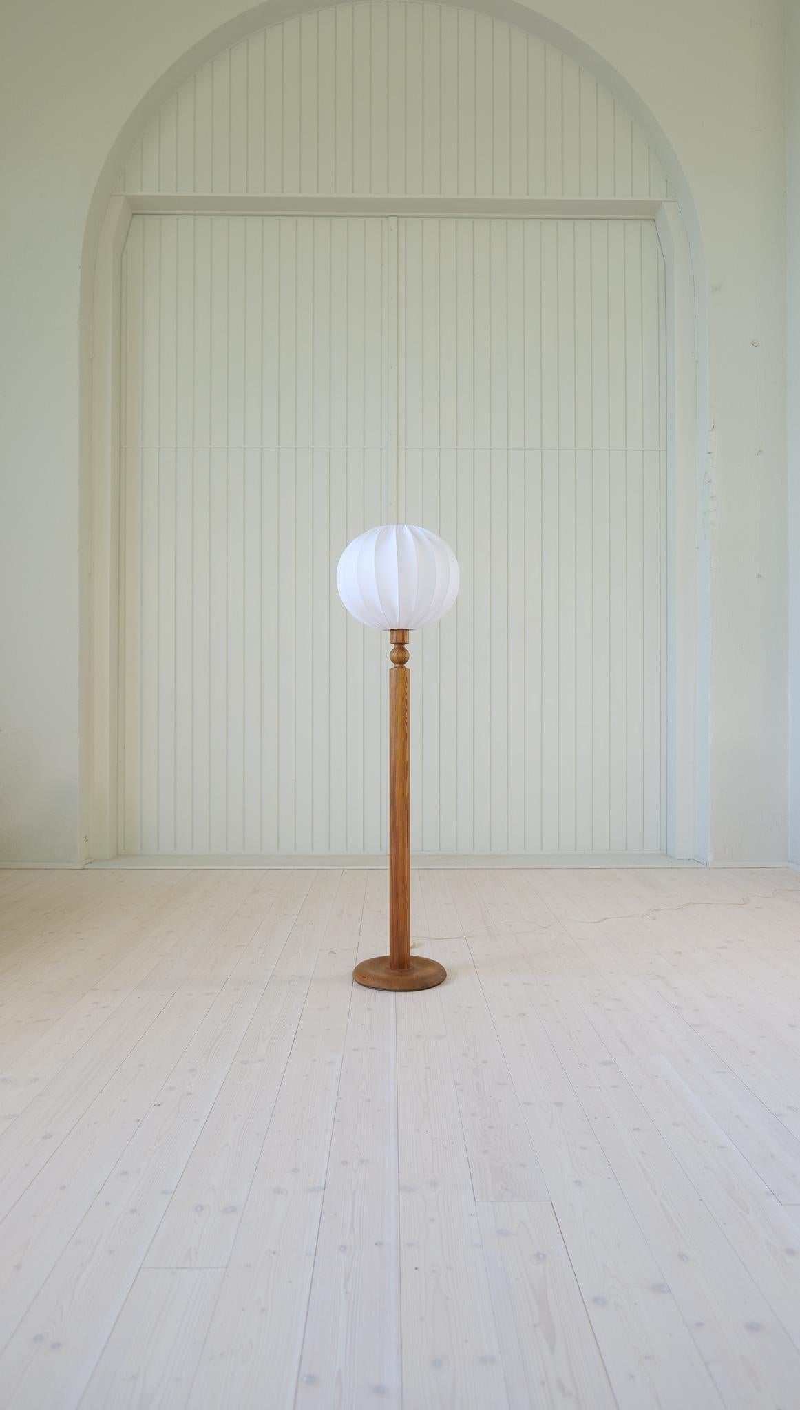 Lampadaire fabriqué en Suède et conçu par Uno Kristiansson. Fabriqué en pin massif, ce meuble à la forme organique confère à votre intérieur une atmosphère agréable. 
Un abat-jour en coton entièrement neuf est inclus. 

Belle condition