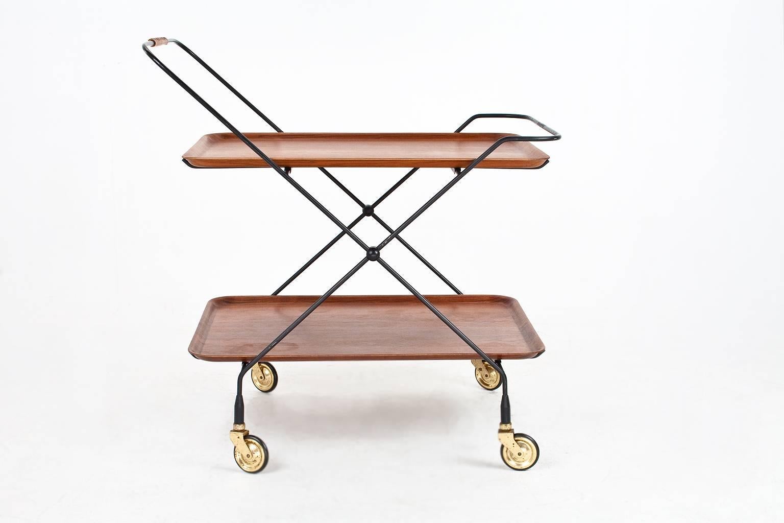 Beautiful Swedish Mid-Century Modern serving table or trolley with two teak serving trays on a black lacquered metal frame with four rotatable wheels. The trolley is foldable as shown on last photo. This piece is in excellent condition, branded