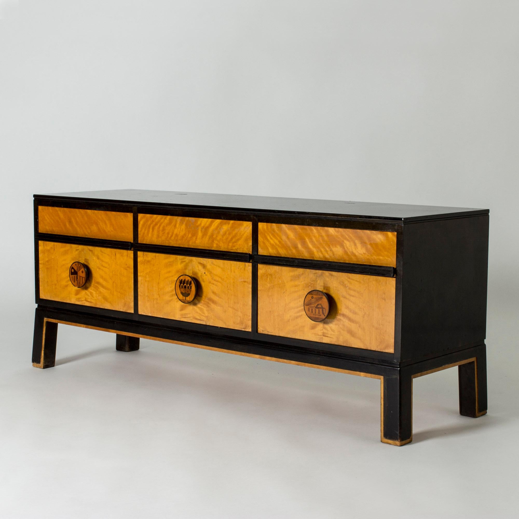 Elegant functionalist sideboard by Otto Schulz, with bold lines and contrasting birch and darker colored wood. Large round drawer handles with decorative inlayed motifs depicting a butterfly, a tulip and a jar with a string of pearls.