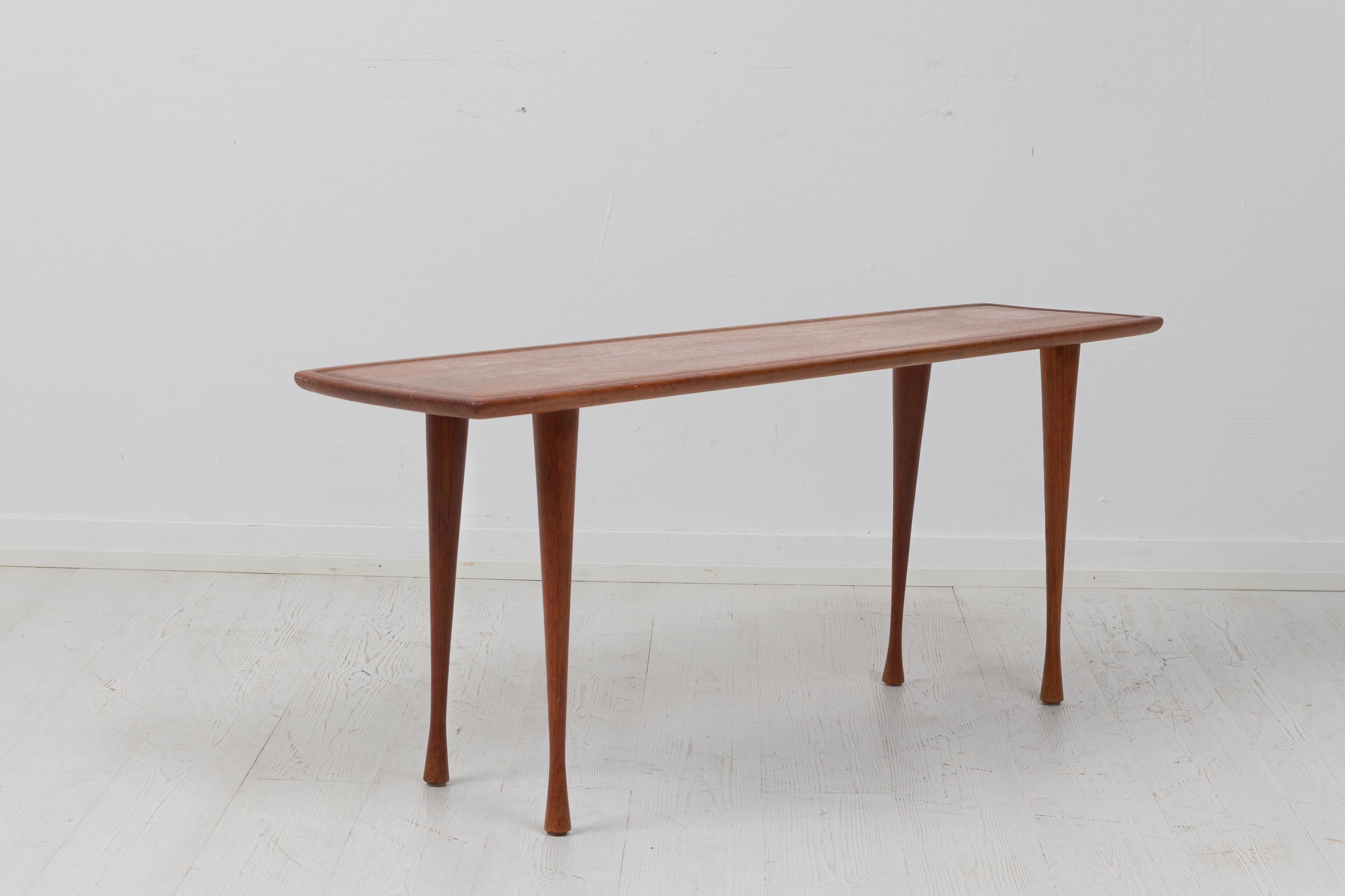 Scandinavian modern teak table from the mid 20th century, around 1960. The table is danish and has a thin and narrow shape. The legs are an elegant touch, they have a slightly irregular shape where they thin out and then curve back again. The table
