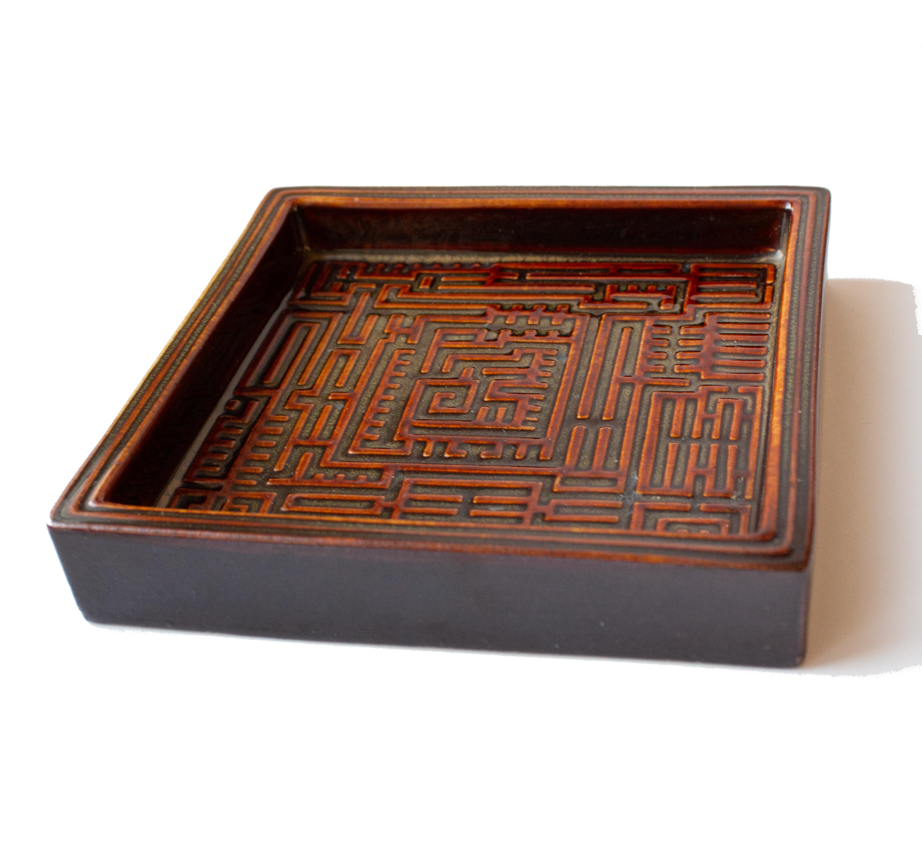 Ce plat carré de la série Domino a été conçu à l'origine en 1954 et présente une glaçure brune avec un motif en relief en forme de labyrinthe en son centre. La série est un excellent exemple de la capacité unique de Stig Lindberg à allier