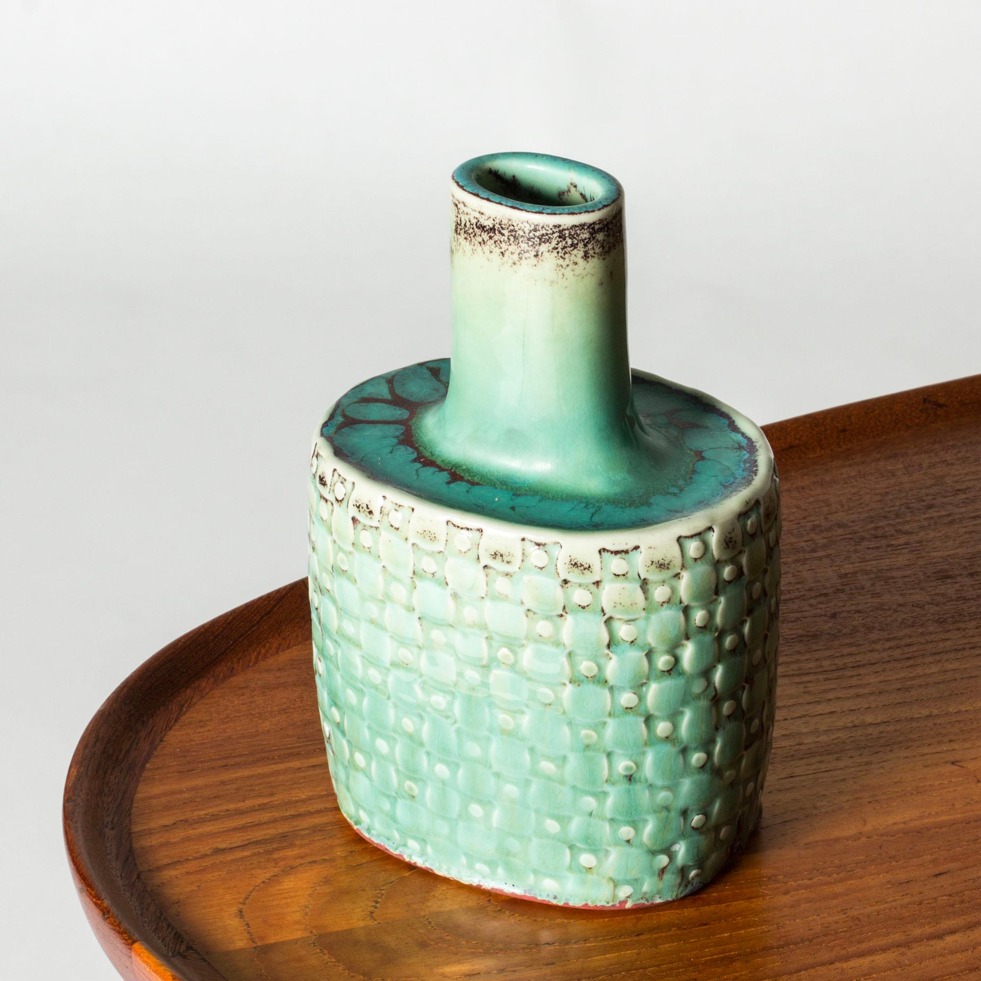 Unique stoneware vase by Stig Lindberg, in a compact flask form, slightly asymmetric. Beautiful embossed graphic pattern, glazed glossy aquamarine with oxblood nuances.