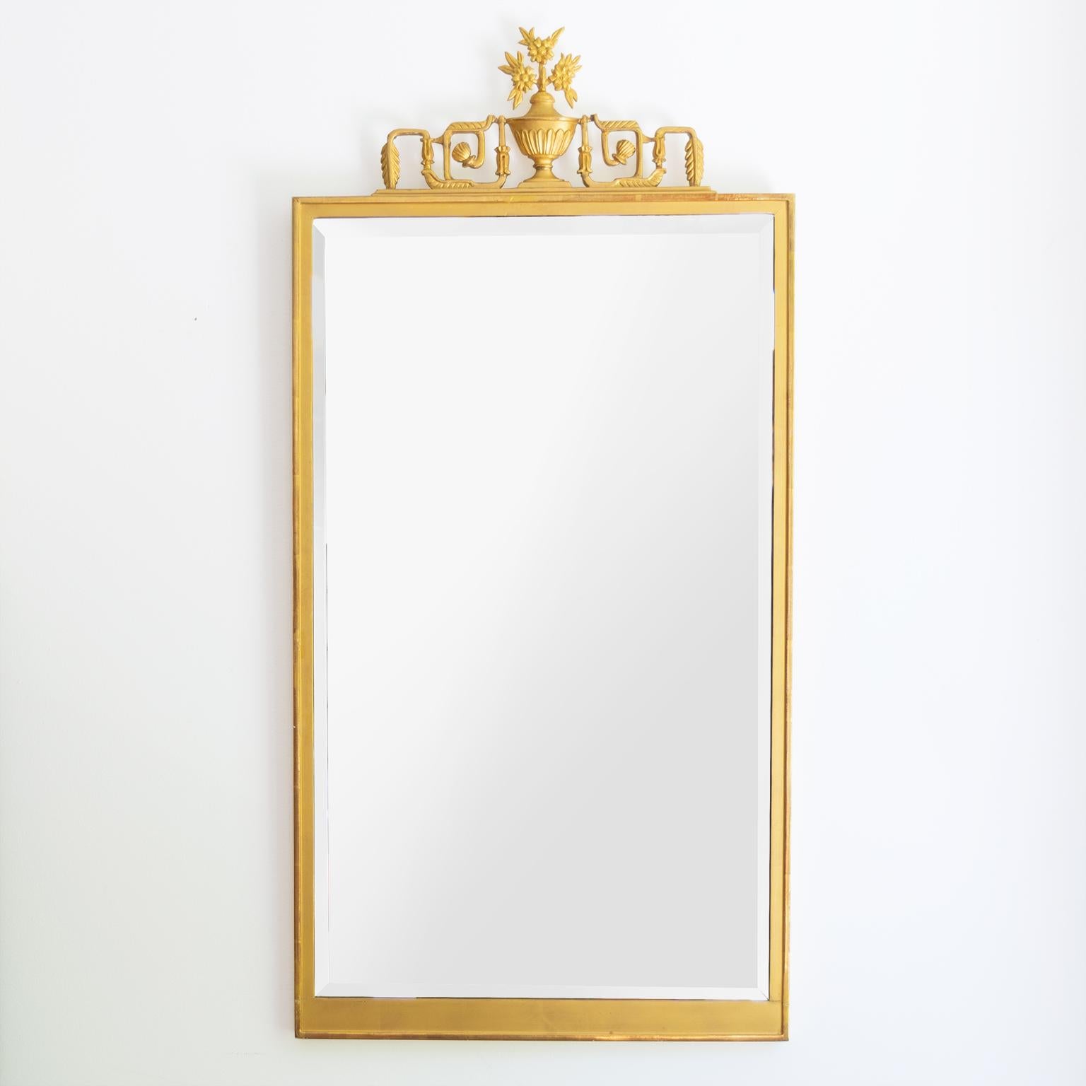 Scandinavian Modern, Swedish Grace, Art Deco giltwood mirror with decorative carving depicting a neoclassical urn flanked by a vine in the form of a meander motif. The mirror retains if original beveled mirror glass resting in a rectangular frame.