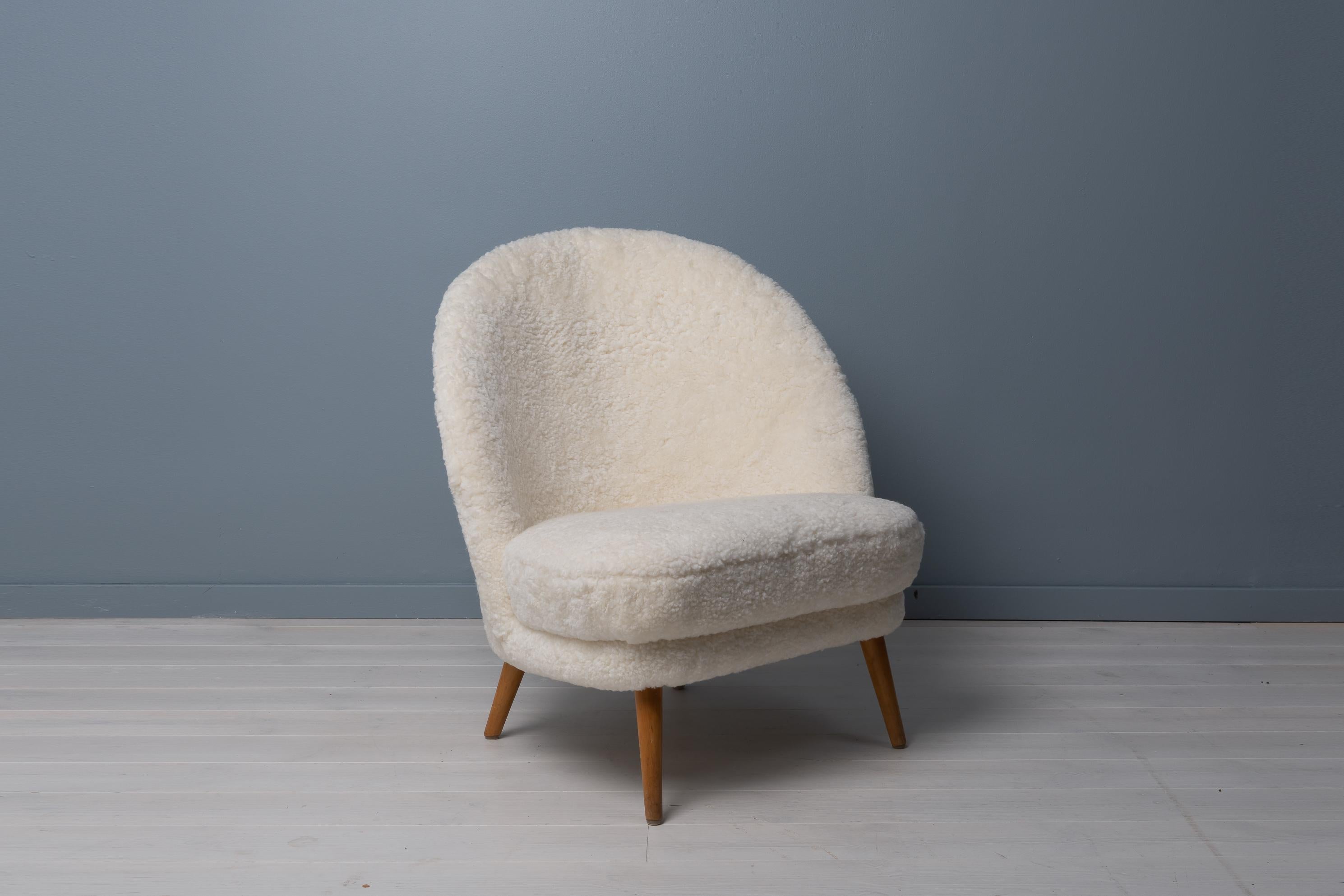 Scandinavian modern sheepskin chair from the mid-20th century attributed to Arne Norell, Sweden. The chair has an asymmetrical back and legs in stained birch. The design is clean and classic with the asymmetry creating extra interest and a twist.