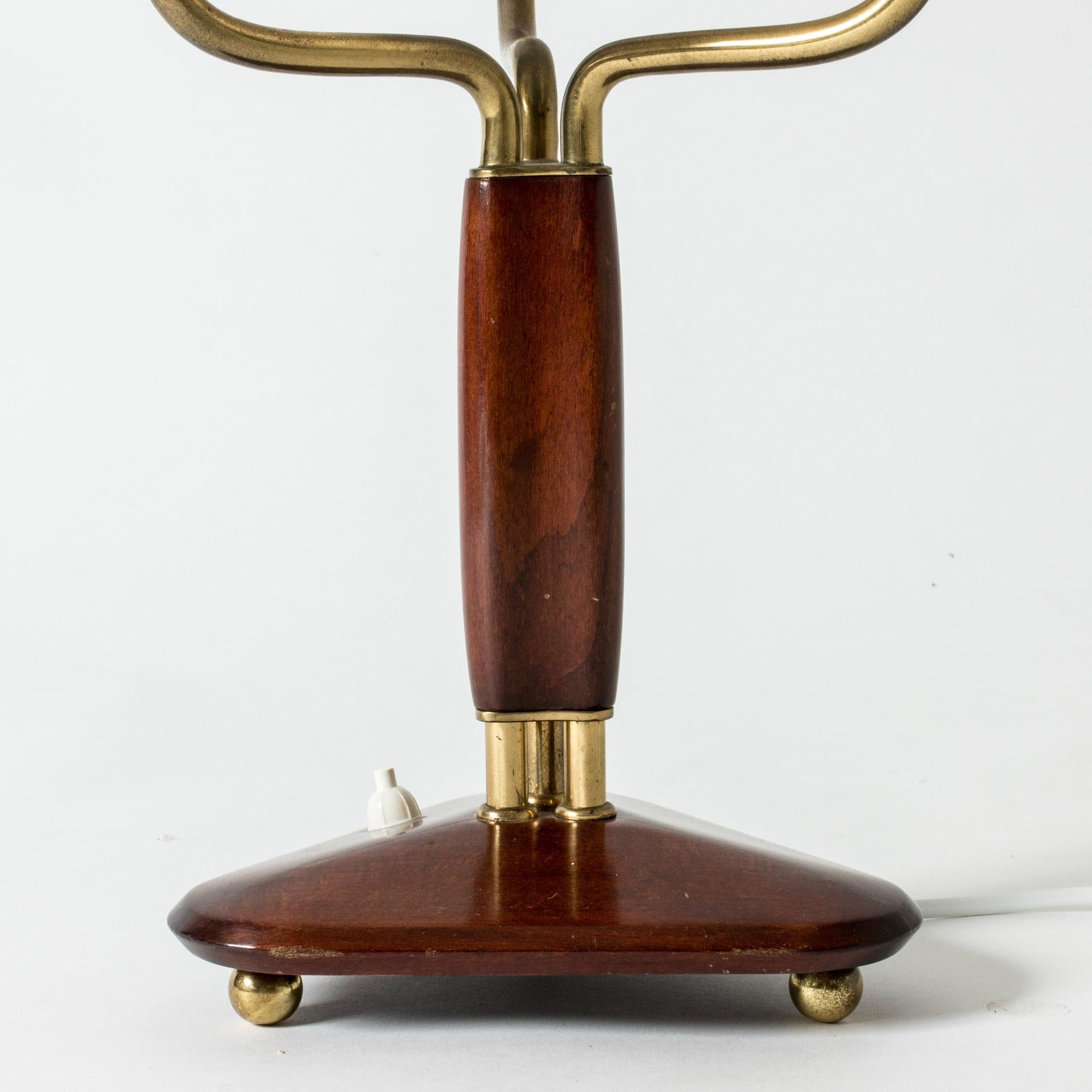 Elegant mahogany table lamp by Carl-Axel Acking, with three brass arms and pleated shades. Triangular base and decorative brass ball feet.