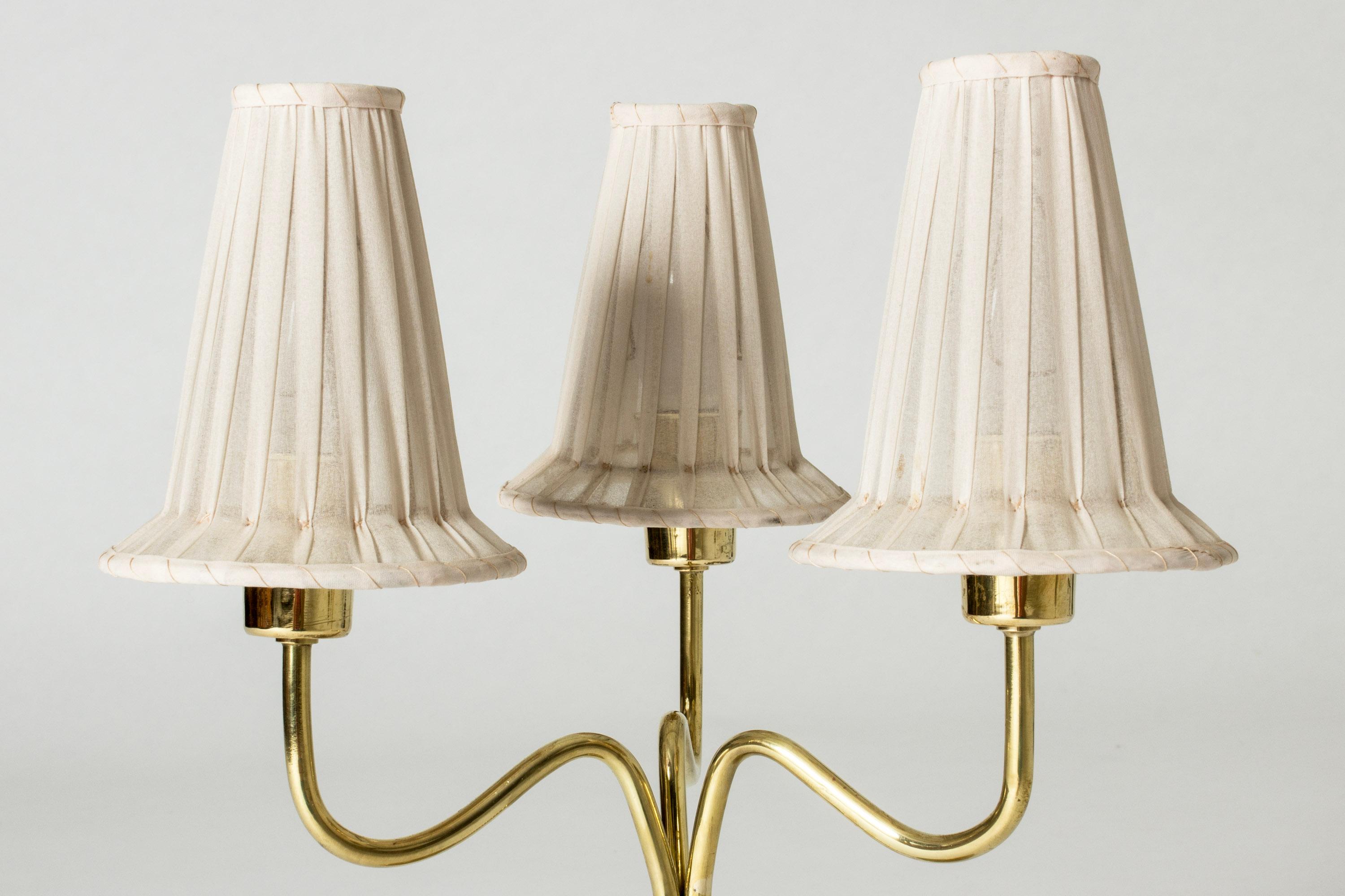 Beautiful, rare table lamp by Hans Bergström, made from brass. Curvesome design with three shades in their original, semi-translucent fabric.

Hans Bergström was the owner and creative director of the lighting firm Ateljé Lyktan, which he founded in