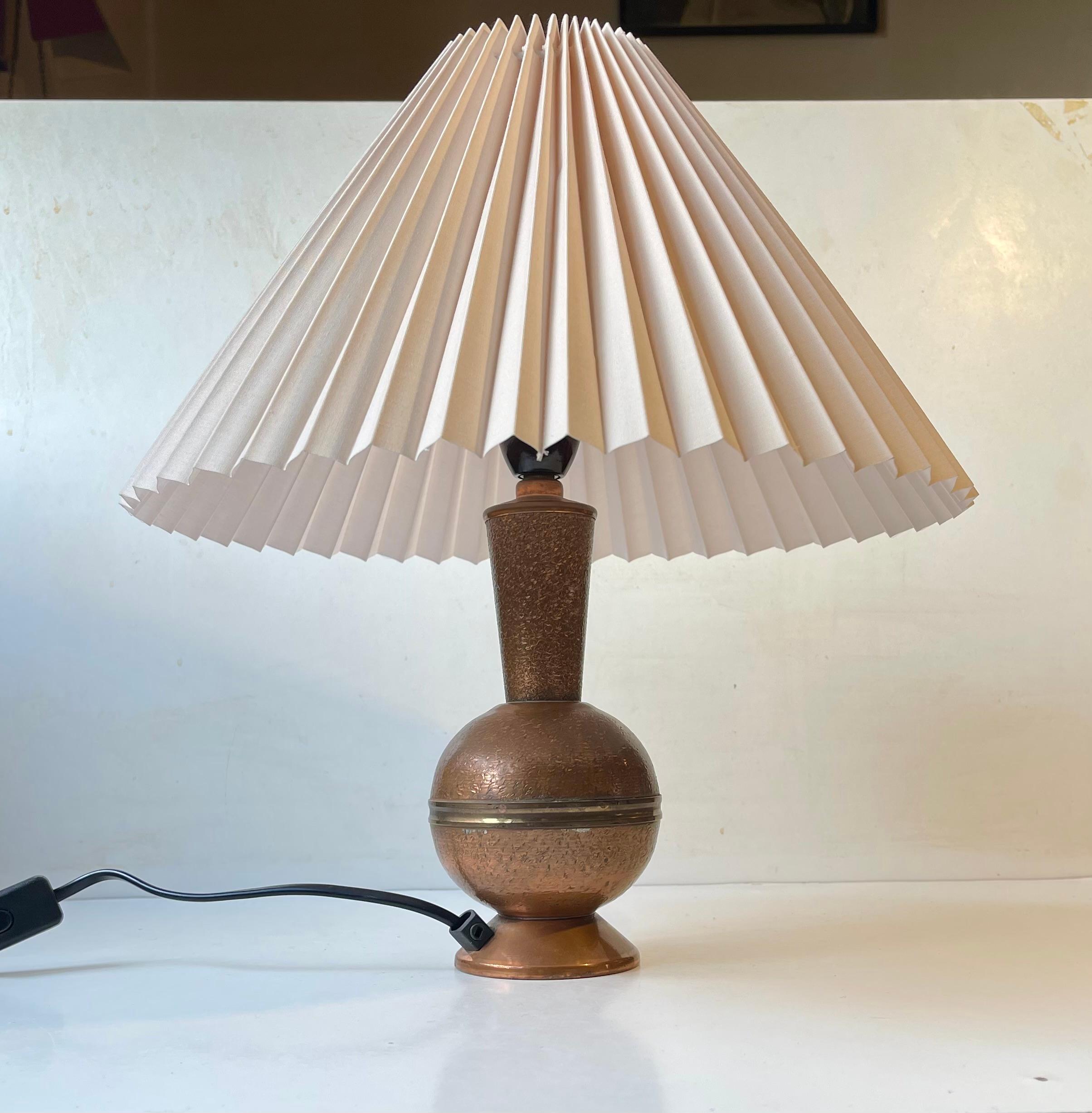 Unusual Table lamp with beige textile shade. The base is fashioned from solid copper with a hammered texture. Unknown Scandinavian maker/designer circa 1950-60. The fluted shade is wellkept and clean.

 Measurements: H: 40 cm (with shade), Diameter:
