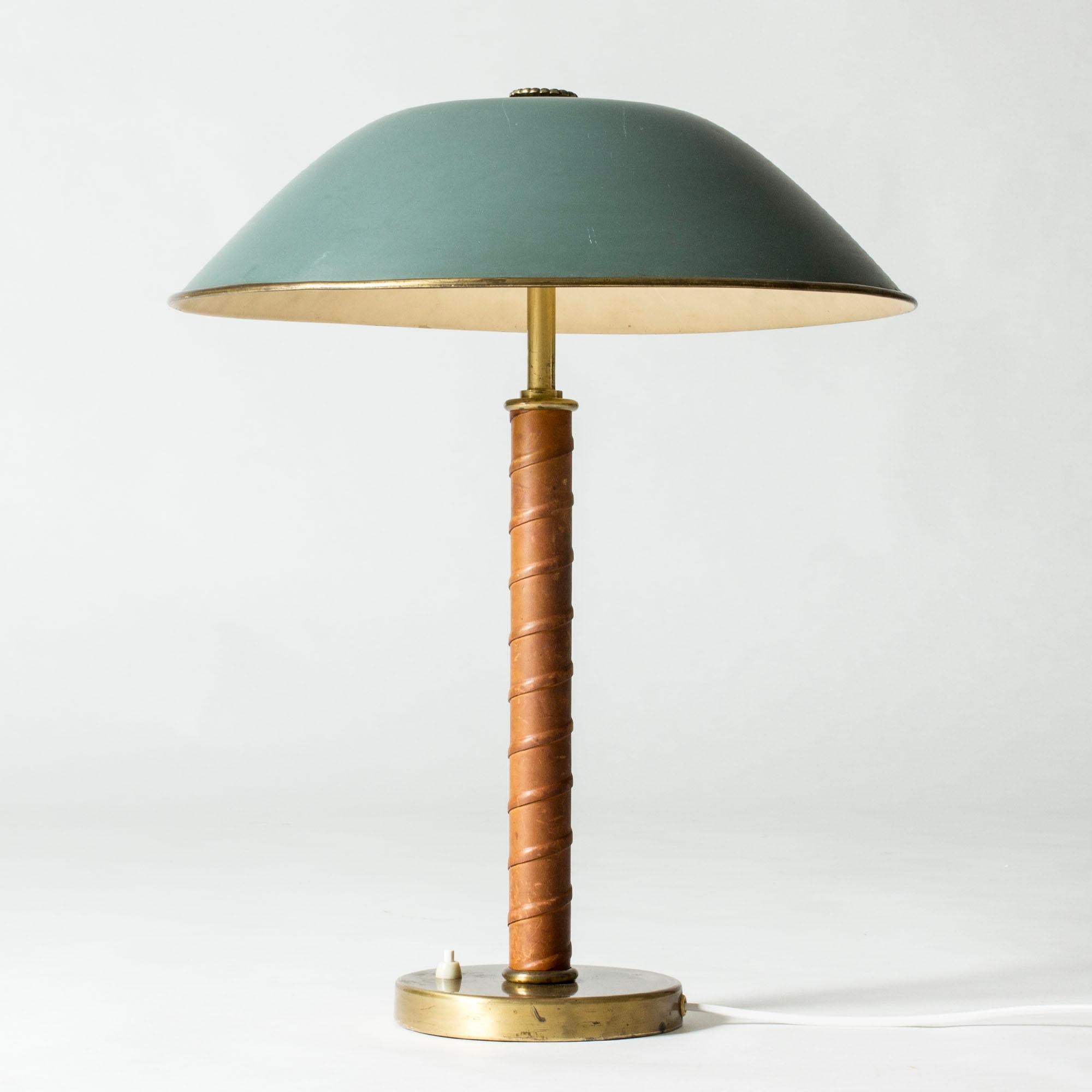 Beautiful table lamp from NK, with a brass base, leather wound handle and green lacquered metal shade adorned with a brass flower.