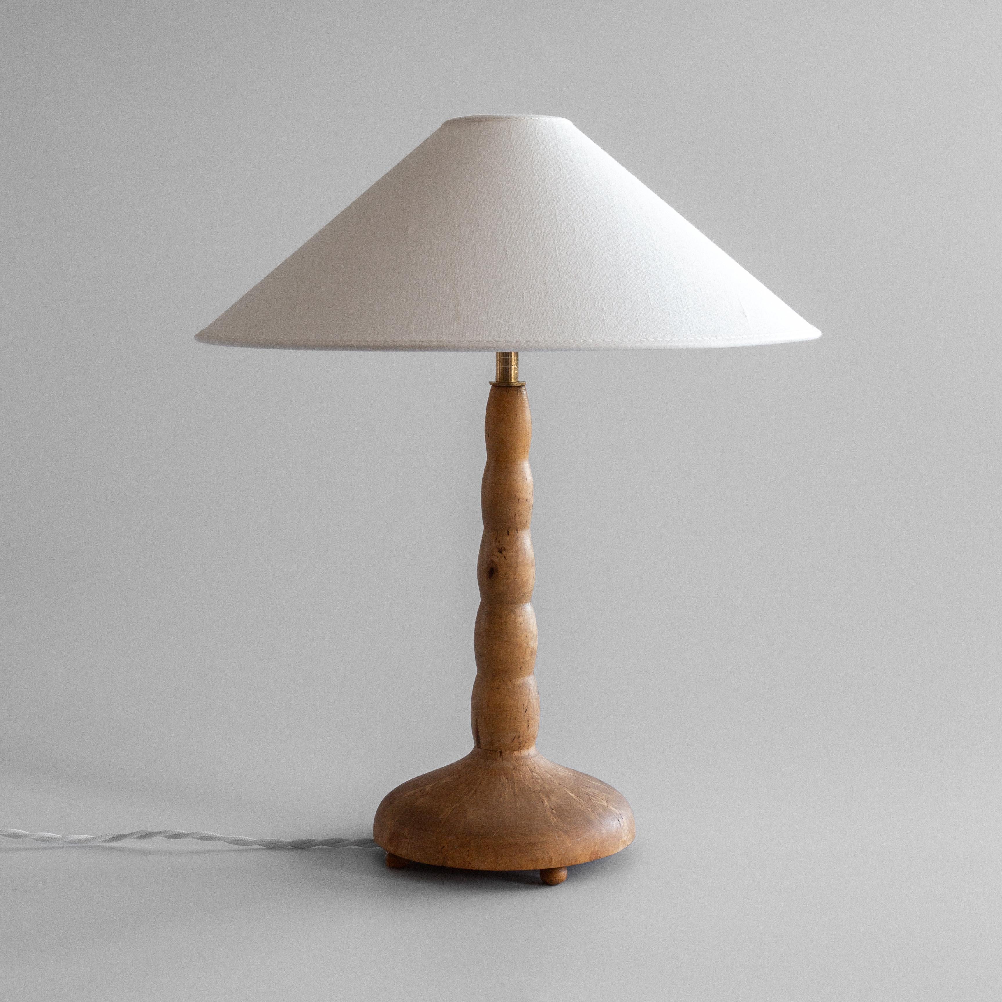 Questa elegante lampada da tavolo moderna svedese degli anni '30-'40 mette in mostra la bellezza senza tempo del design scandinavo. La lampada presenta uno stelo di betulla meticolosamente tornito a mano con curve organiche e aggraziate che creano