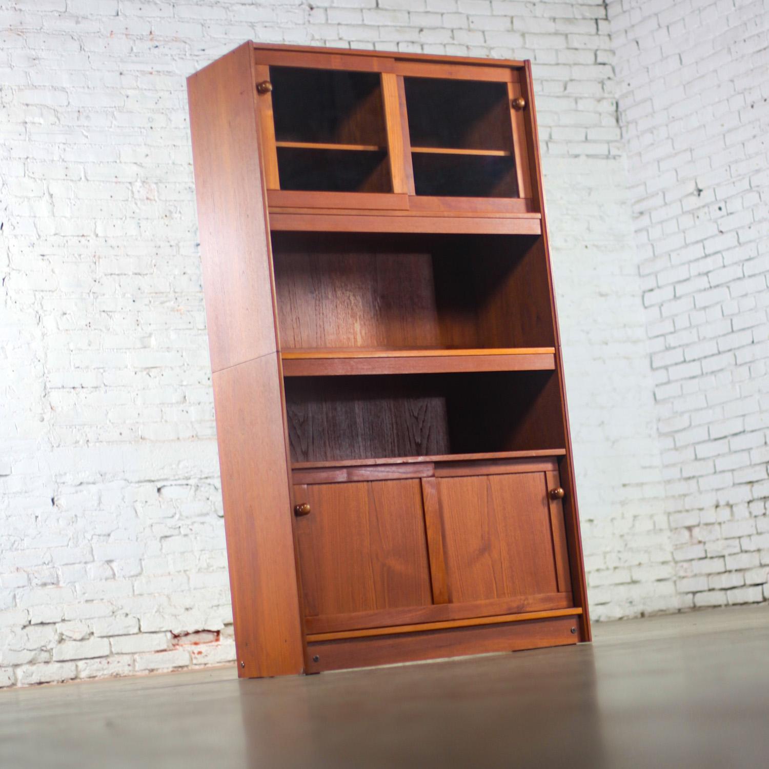 Marvelous Mid-20th Century Scandinavian Modern teak display cabinet, bookcase, or sideboard stamped “Made in Denmark” & comprised of 2 pieces. Upper display hutch w/double doors, glass insert fronts, round teak knob pulls, & 1 adjustable wood shelf.