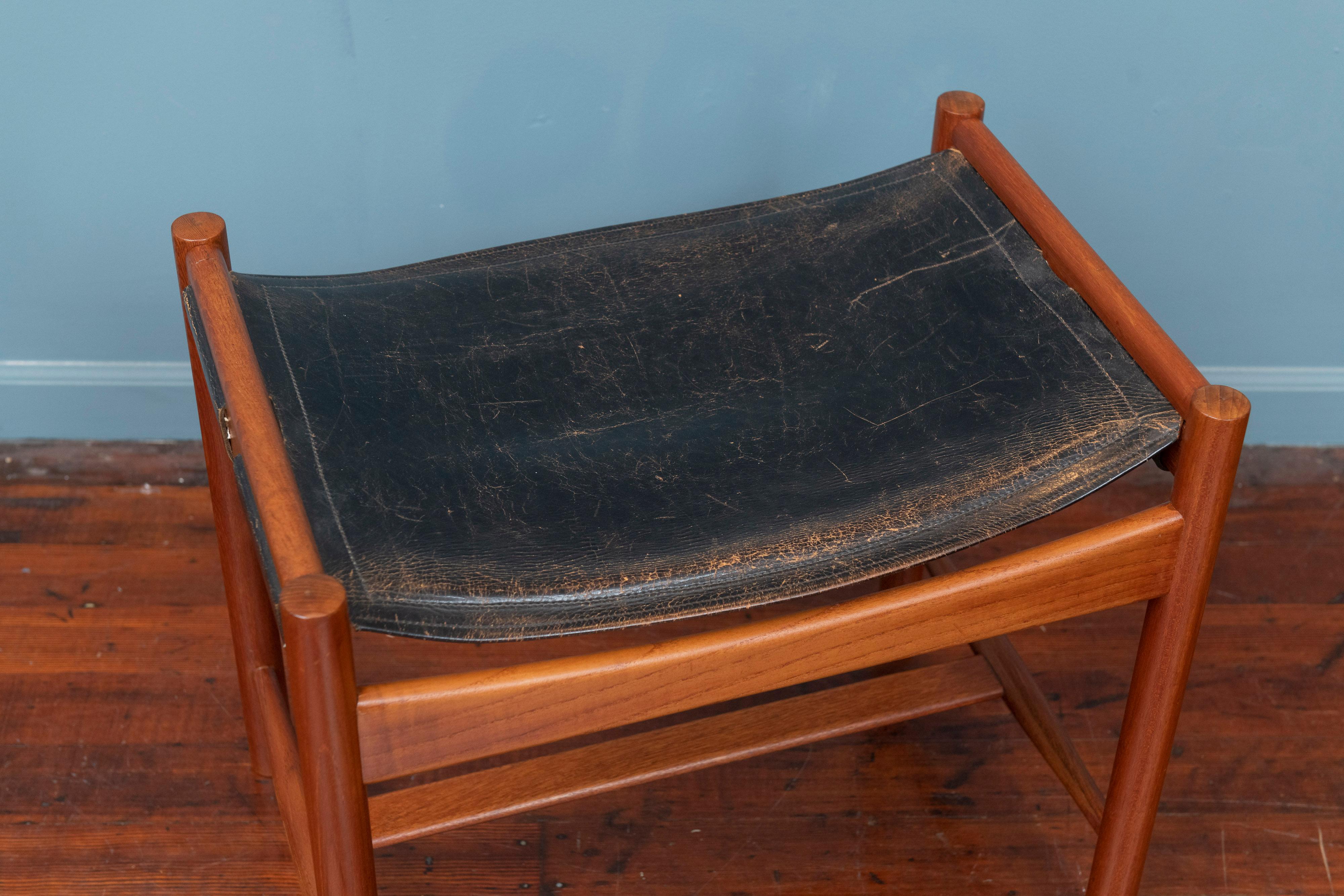 Scandinavian Modern design footstool by Kurt Olsen, Denmark. Newly refinished teak frame with its original black leather seat, having a warm worn patina to it that is stable and secure enough for daily use. Having rounded legs and shaped cross