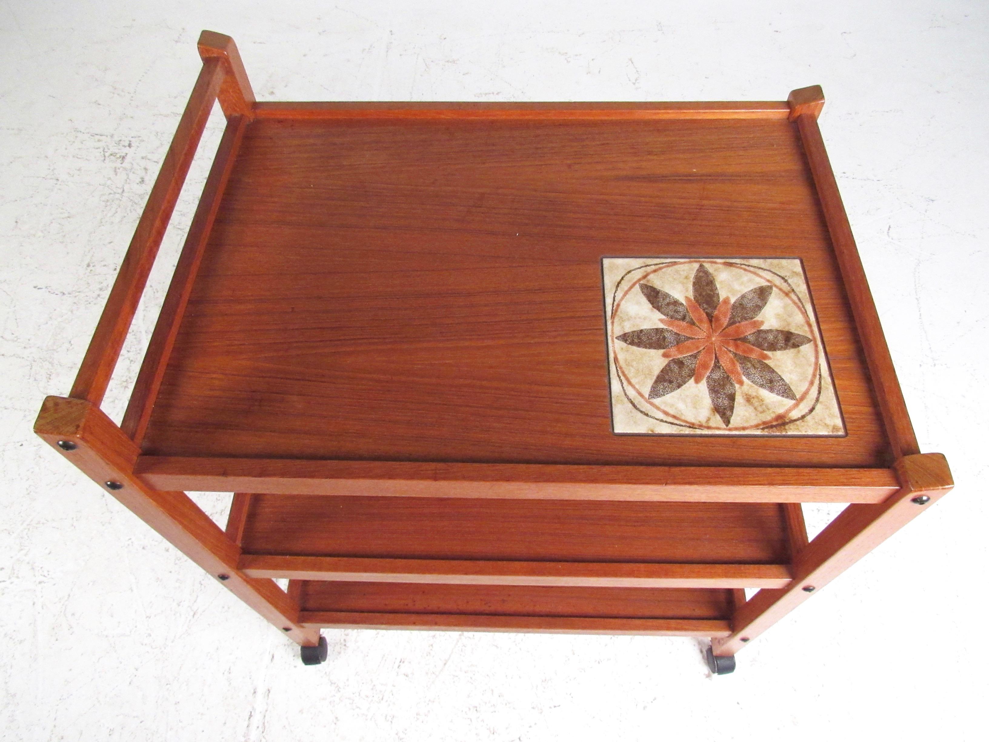 This stylish Mid-Century Modern service cart features a striking teak finish with unique painted tile inlay. Perfect vintage trolley or bar cart, ideal for storage, display, or serving. Please confirm item location (NY or NJ).