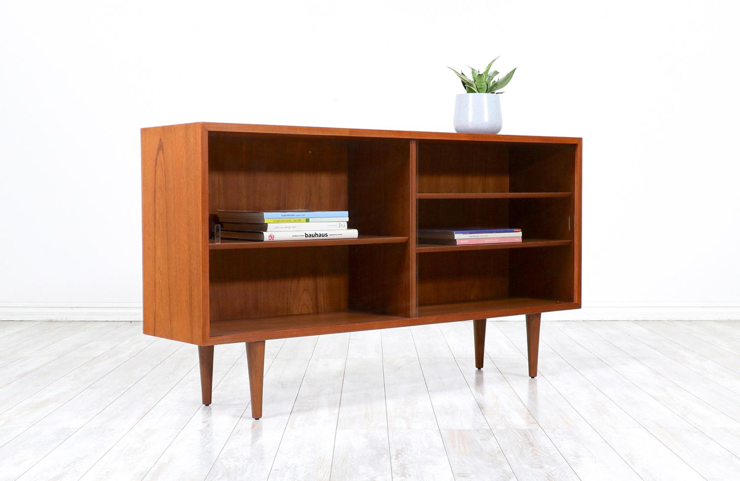 Stylish Danish credenza designed for Carlo Jensen for Hundevad & Co. in Denmark circa 1960s. This sleek design features a teak wood case sitting on four tapered legs with its original sliding glass doors. The interior is comprised of two