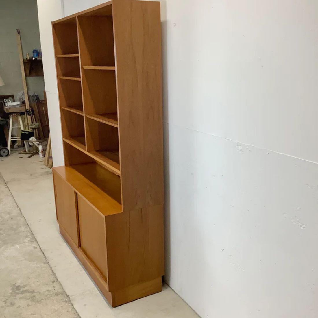 This vintage danish teak bookcase features two piece design combining adjustable upper shelves with lower sliding door cabinet storage. Perfect array of storage options for dining room service, living room media storage, or for use as an office