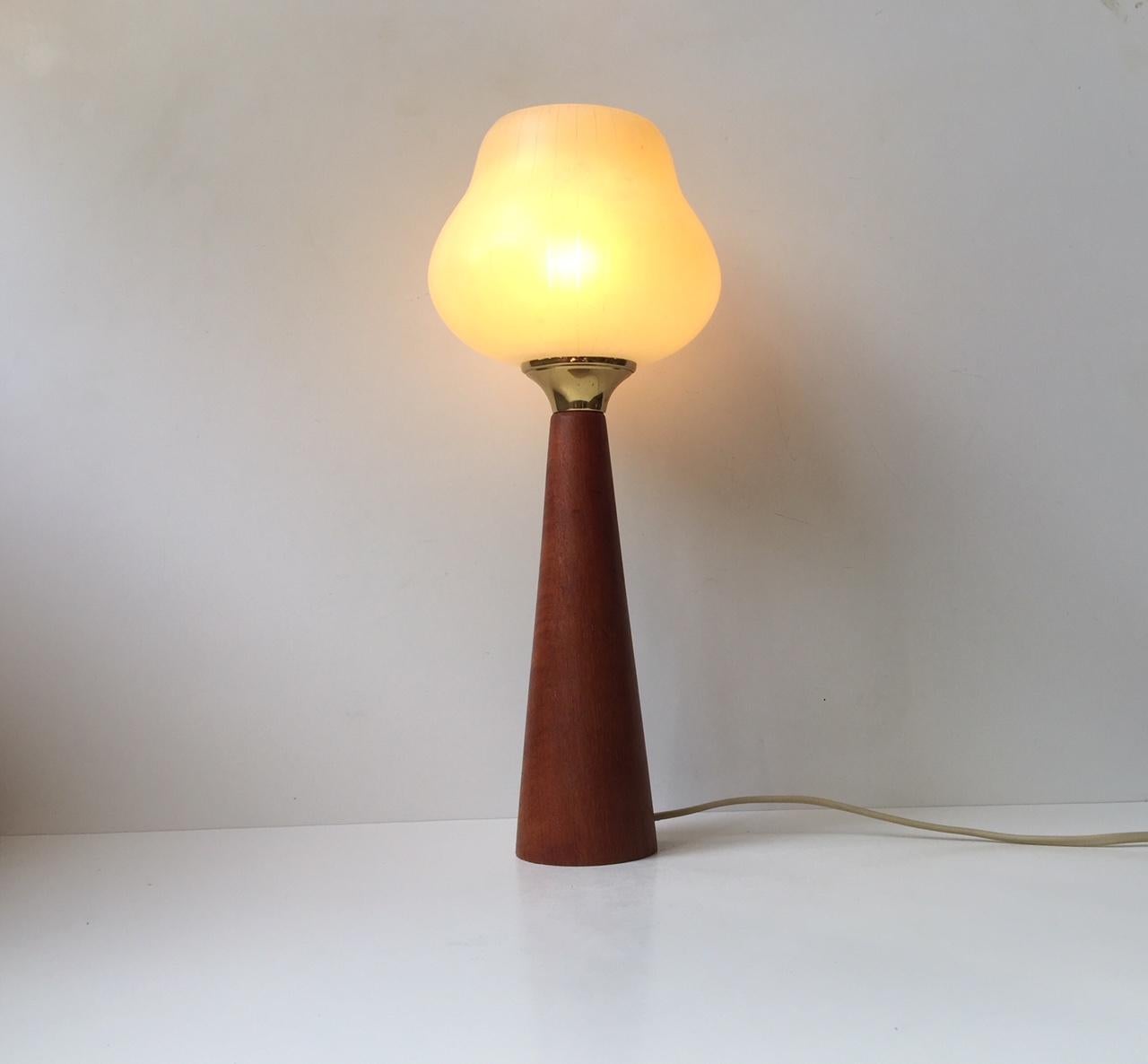 A table lamp composed of a conical solid teak base, a brass socket and a pin-striped single layered glass shade in an organic shape. It was made in Scandinavia during the 1960s in a style reminiscent of Gino Sarfatti.