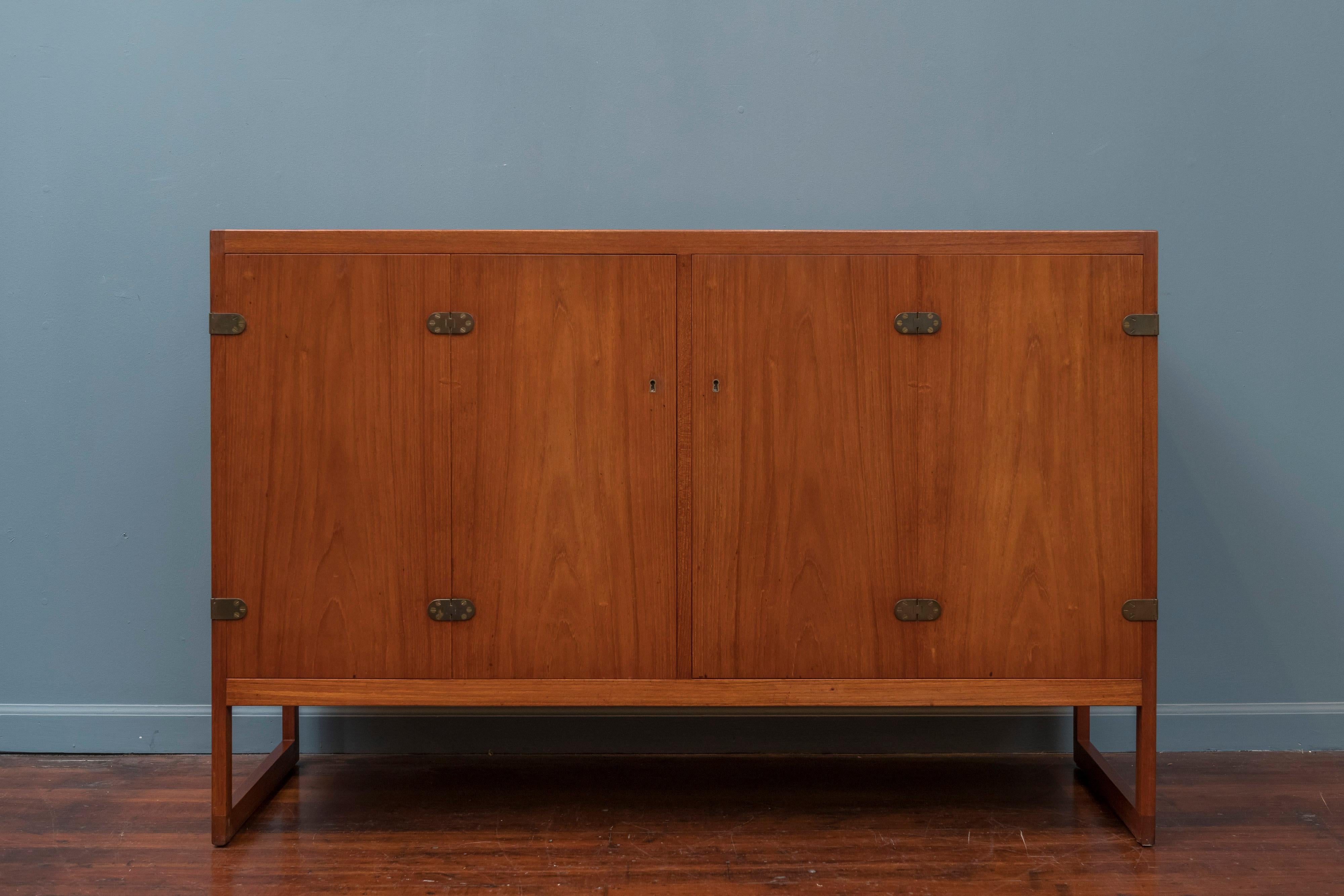 Scandinavian Modern teak cabinet, elegantly understated and designed by Borge Mogensen for P. Lauritsen and Son. Two bi-fold doors open to reveal four oak finger-jointed drawers and two shelves. The exposed brass hinges on this piece add just the