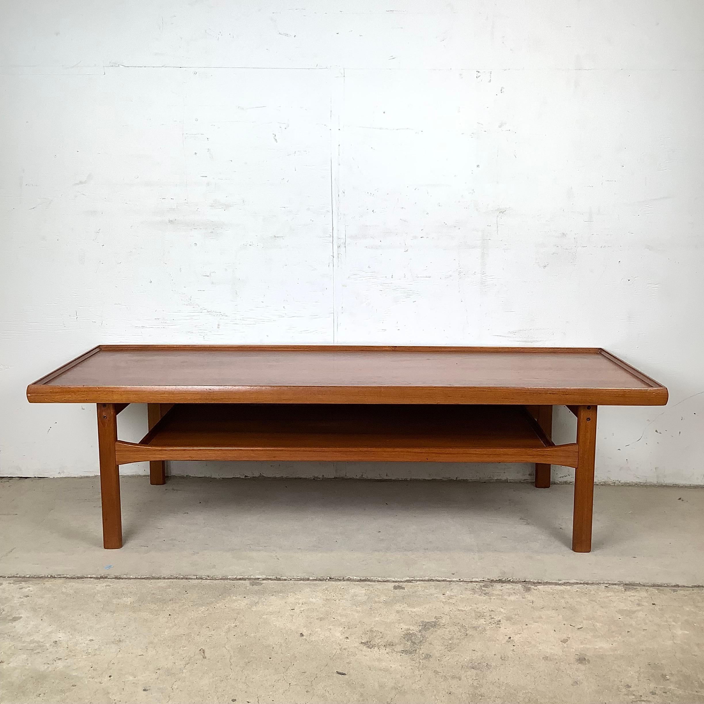 Der hier angebotene Couchtisch aus Teakholz aus der Mitte des Jahrhunderts im Stil von Moreddi verfügt über einen erhöhten Rand und eine untere Ablage aus Teakholz. Das Design ist zwar nicht gekennzeichnet, spiegelt aber die klaren Linien und die