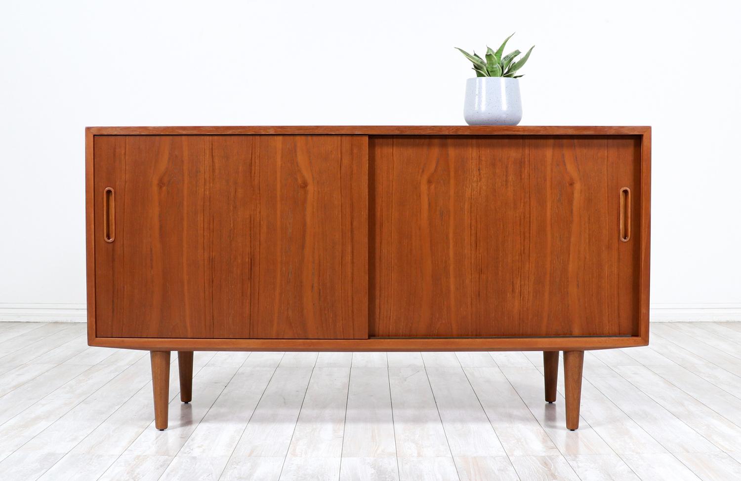 Compact Danish Modern credenza designed by Carlo Jensen for Hundevad Co. in Denmark circa 1960s. This compact credenza features a solid teak wood case with a birch wood interior and two doors that open smoothly revealing ample storage space. The