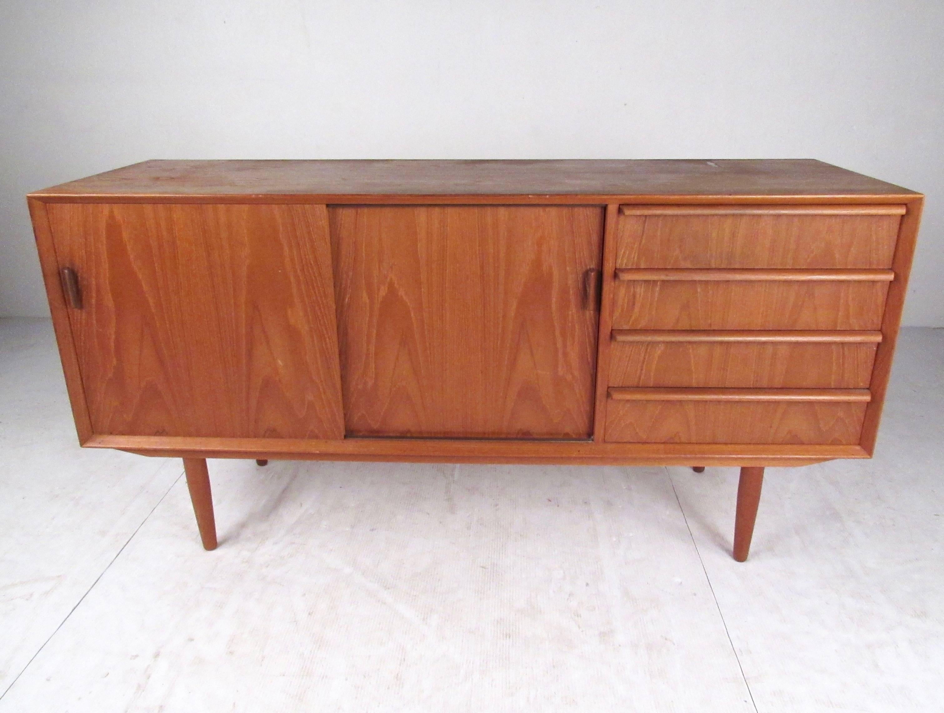 This stylish Danish modern credenza by Falster makes a stylish storage cabinet for home or office storage. A versatile mix of storage includes sliding door cabinets and dovetailed drawers, this small-scale credenza features carved pulls and rich