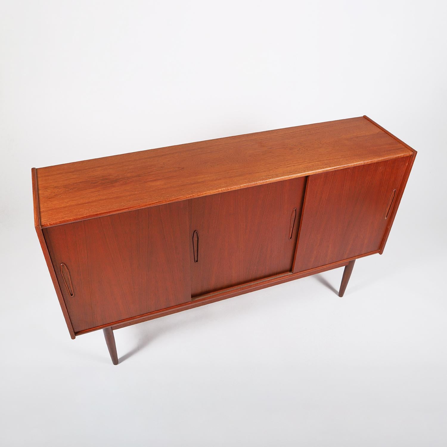 A vintage original Scandinavian Modern sideboard in rich old growth teak with a traditional oil finish. Turned legs, sliding doors with diamond shaped pulls, adjustable shelves, interior etched glass mirrored bar and beechwood trimmed silver