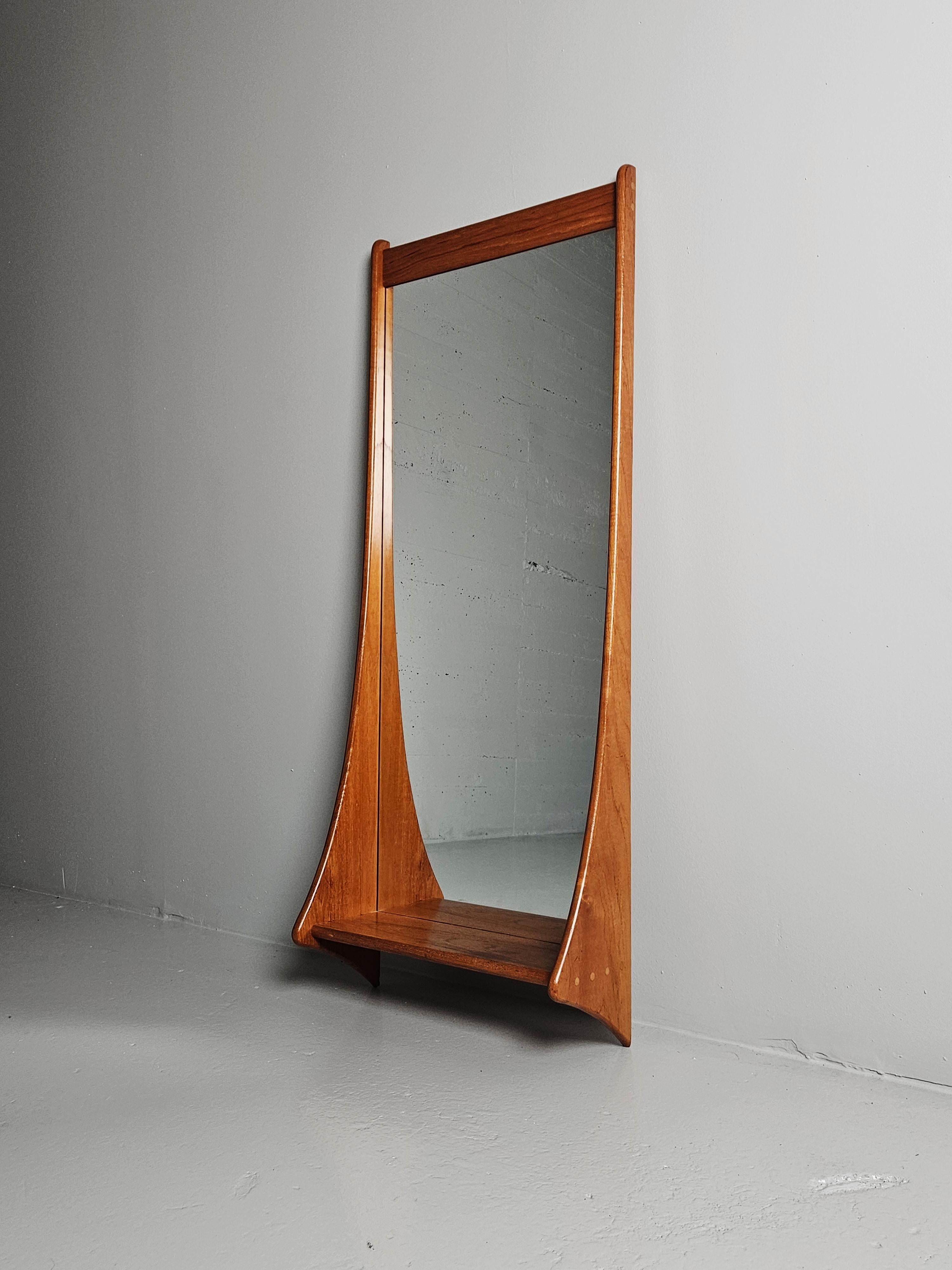 Magnifique miroir d'un designer inconnu, fabriqué au Danemark dans les années 1960. 

Fabriqué en teck massif avec une étagère à chevilles décoratives. 