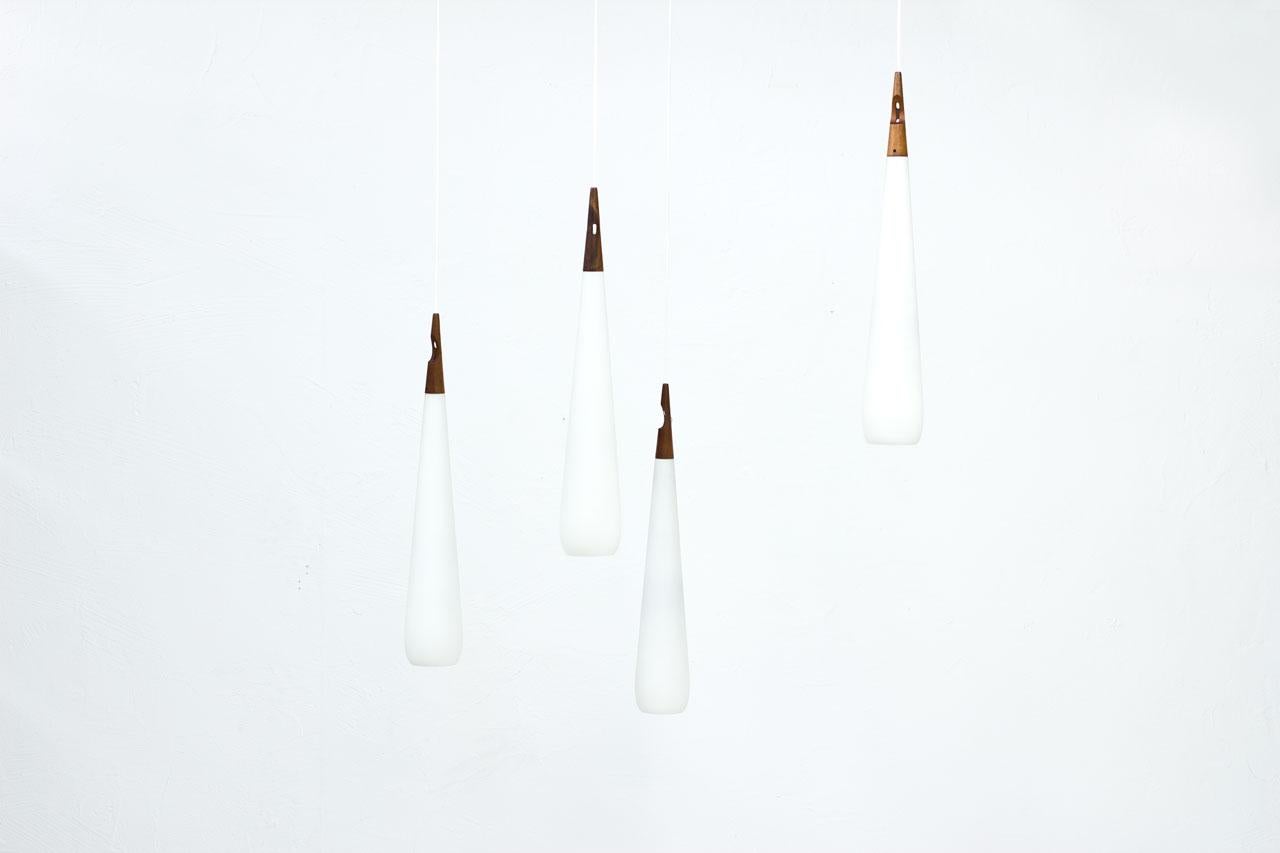 Pendant lamps model “Droppe”  (the drop) designed by Uno & Östen Kristiansson, manufactured by their own company Luxus in Sweden during the 1950s.
The lamps are made from a long drop shaped opaline glass with teak fitting. 
Electricity has been