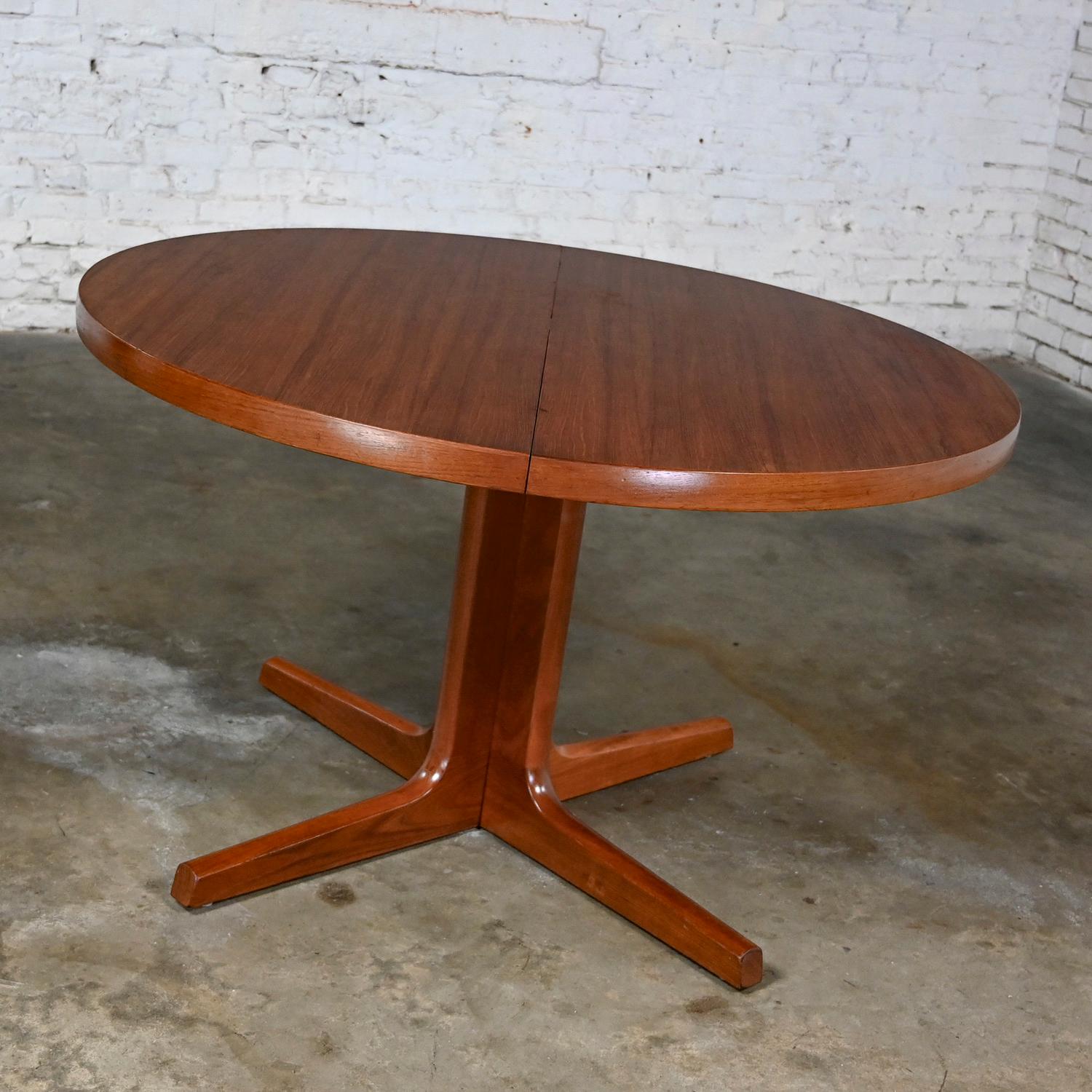 Handsome Mid-20th Century Scandinavian Modern teak round to oval extension dining table with pedestal base and 2 leaves by Ansanger Mobler. It bears the AM Made in Denmark stamp on its underside. Beautiful condition, keeping in mind that this is
