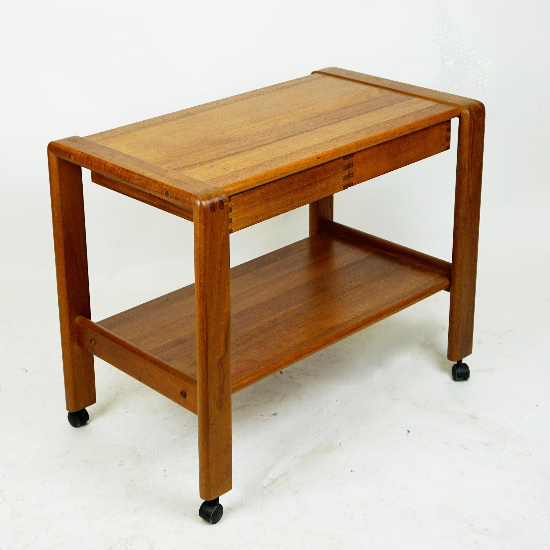 This charming Scandinavian Modern teak serving table or bar cart has been designed and produced in Denmark, 1960s.
It features beautiful handcrafted details, two trays and two drawers under its top. It is in beautiful original vintage condition and